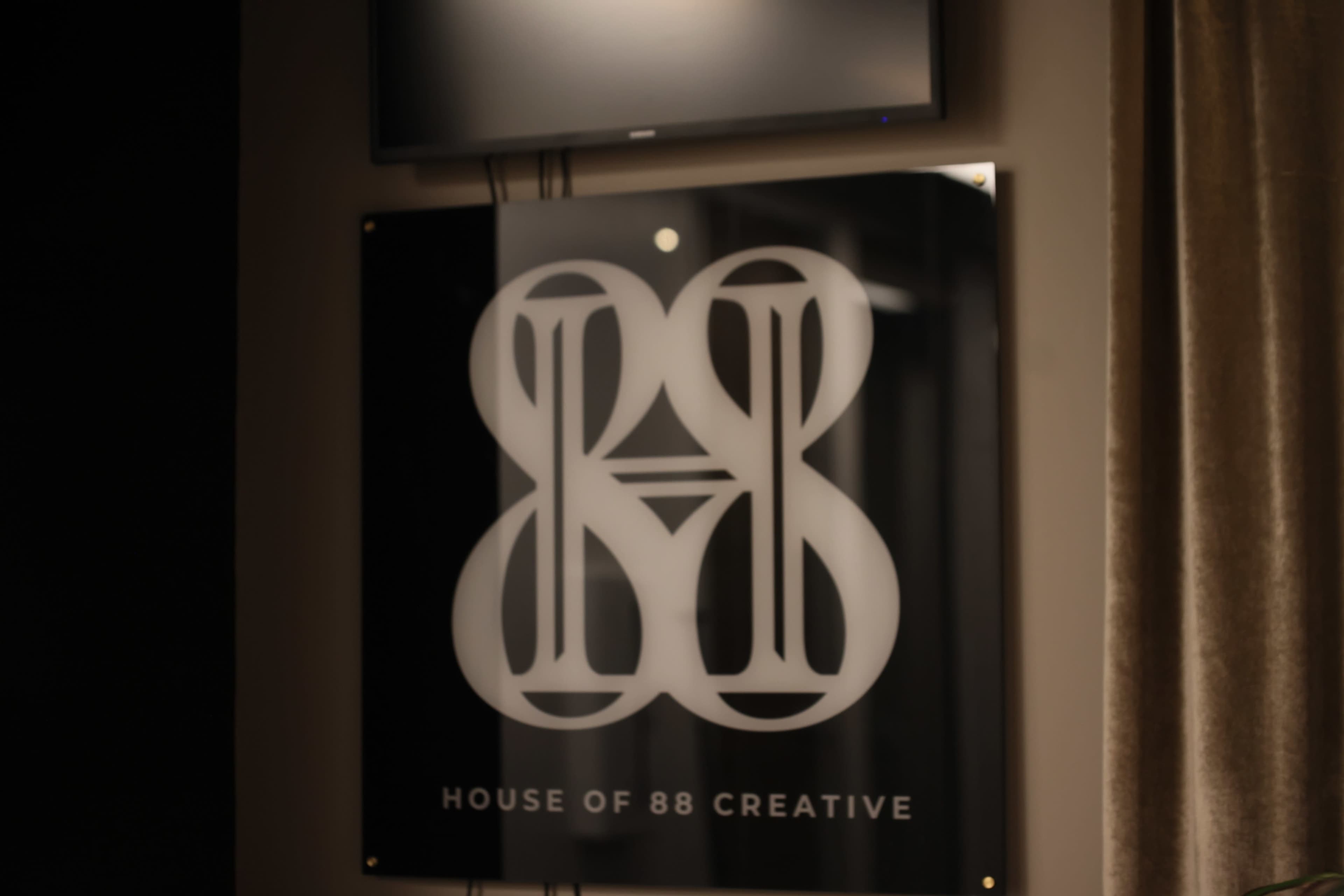 The image shows a modern sign displaying the logo of "House of 88 Creative" on a wall with a television mounted above it.