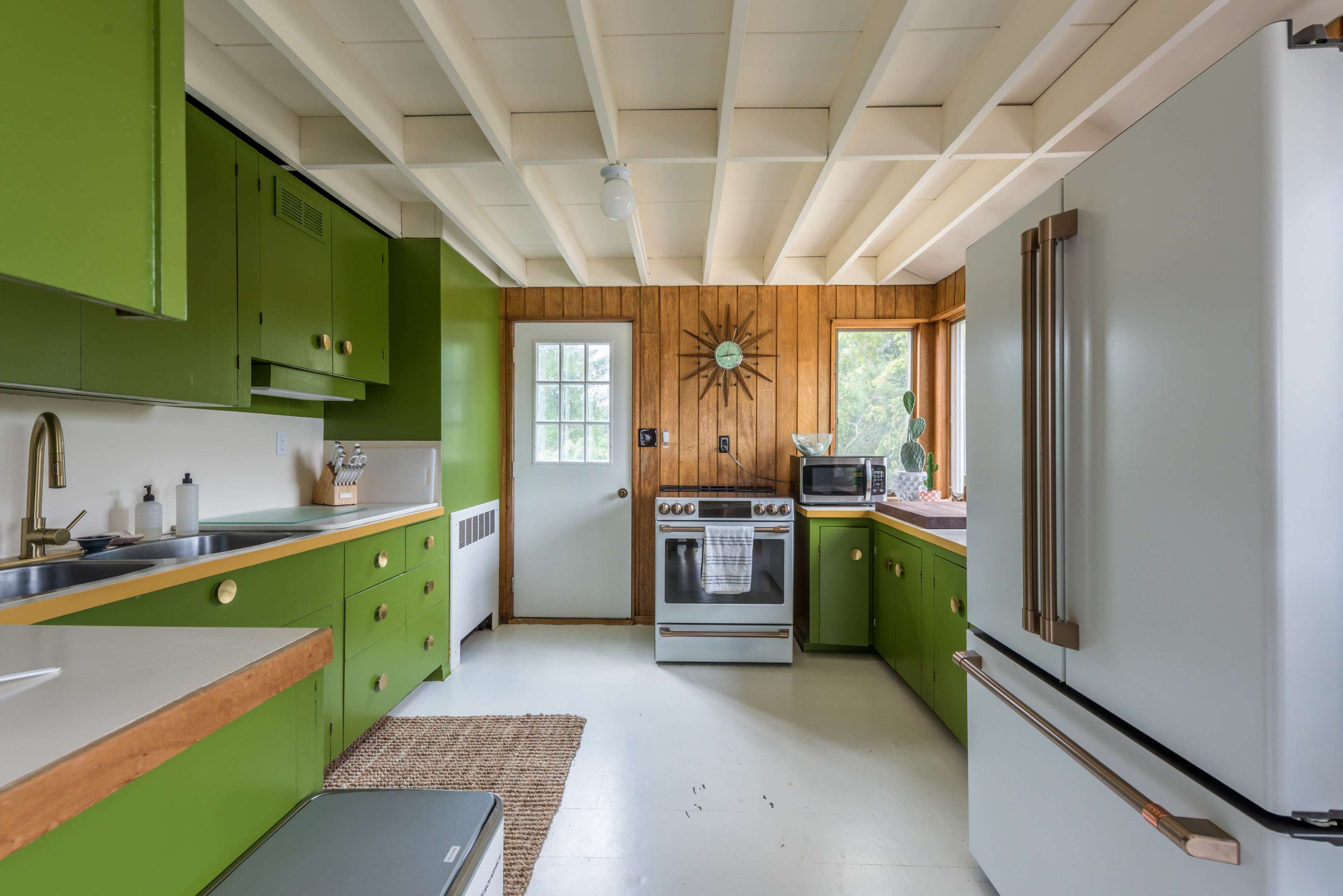 The kitchen features green cabinets, a white stove and refrigerator, and a wood-paneled wall with a window.