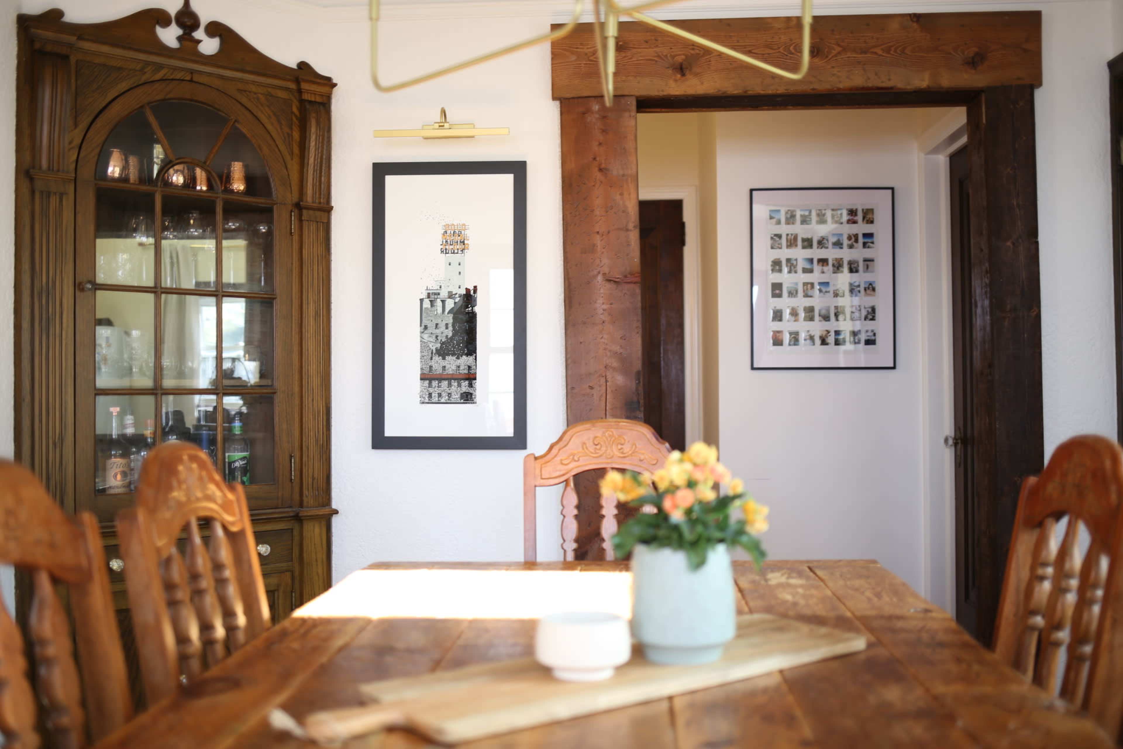 A dining room features a wooden table with chairs, a glass-fronted cabinet displaying items, and framed art on the walls.
