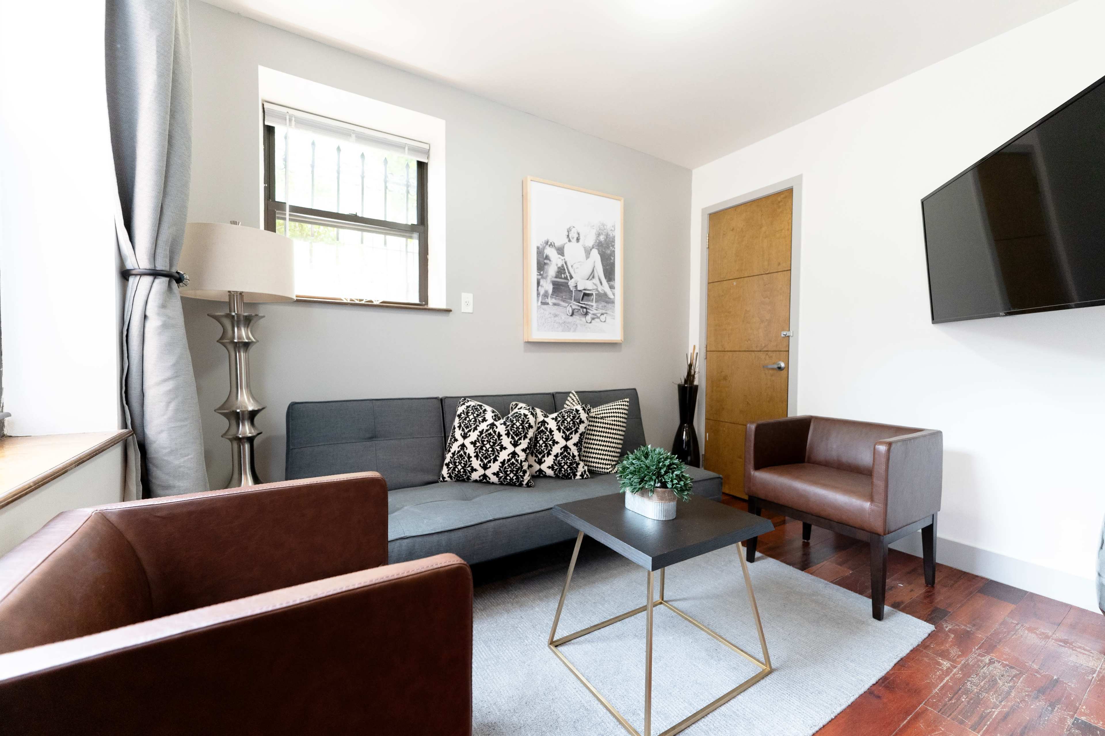 A modern living room with a gray sofa, two brown chairs, a coffee table, and a television mounted on the wall.