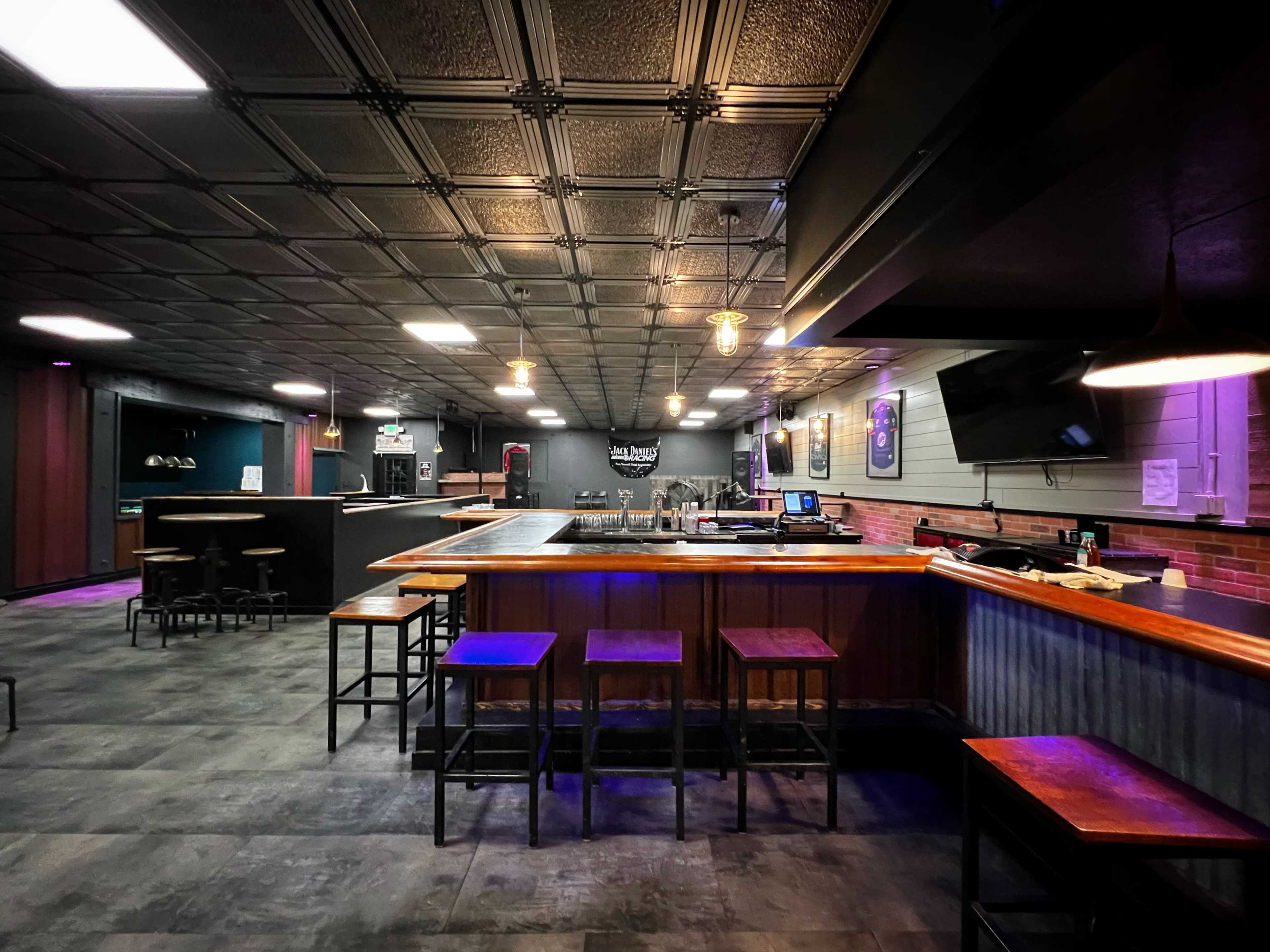 An empty bar area with high stools, dim lighting, and a modern design featuring a gray and wood color scheme.