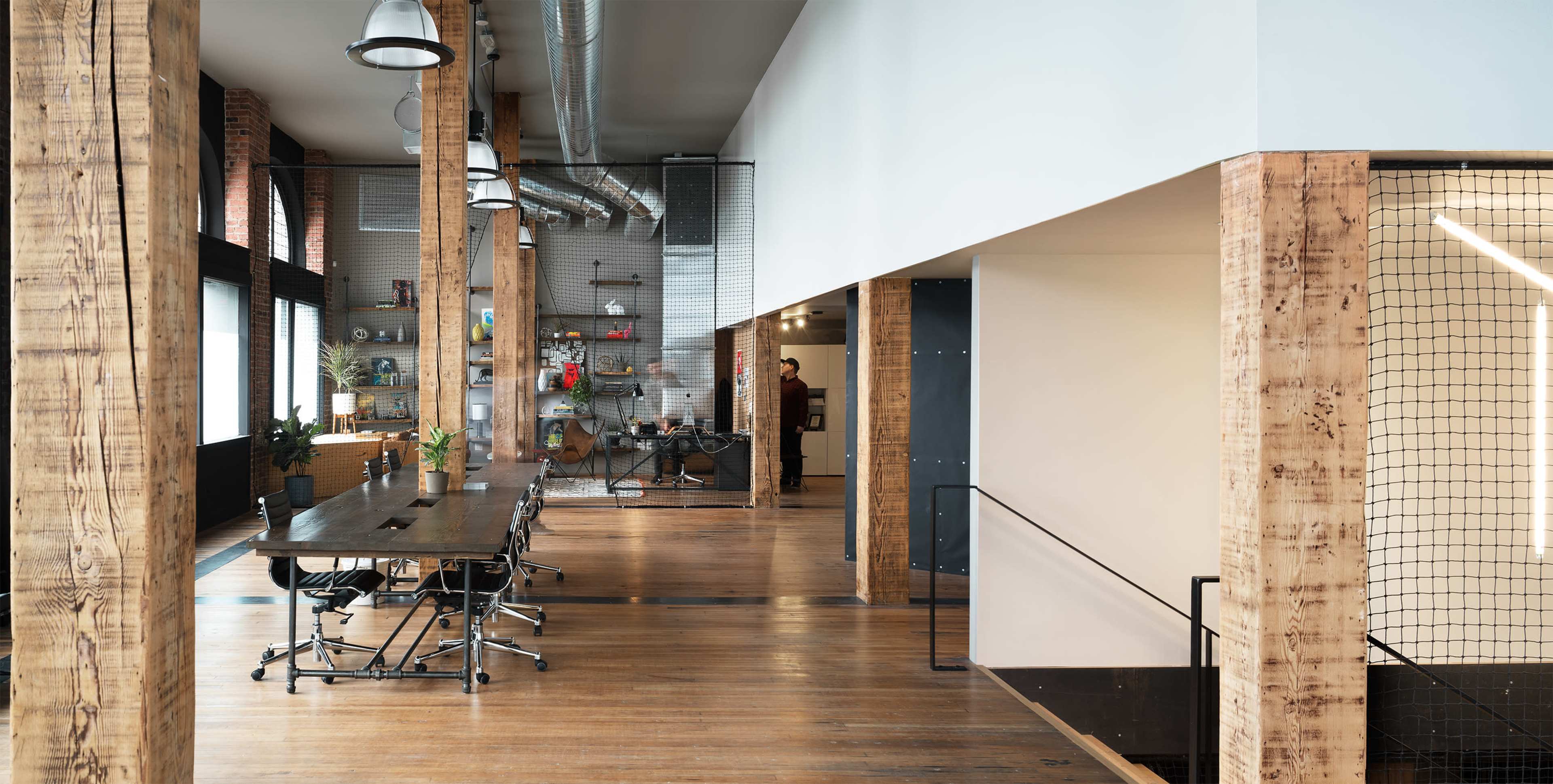 The image shows a spacious, modern office with wooden beams, a large conference table, and open areas featuring industrial design elements.