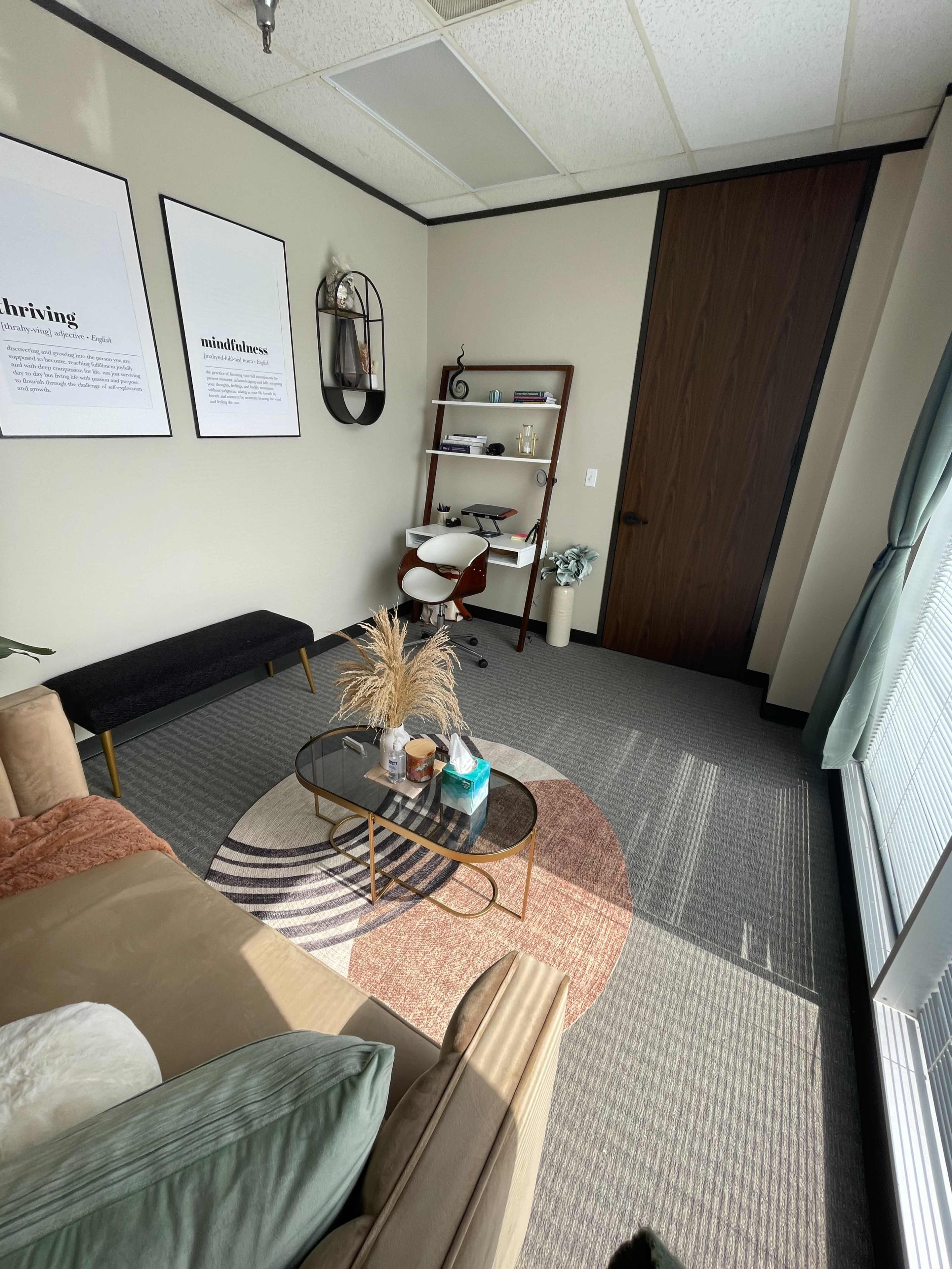 A neatly arranged office space featuring a small seating area with a couch, a coffee table, a desk with a chair, and decor on the walls.