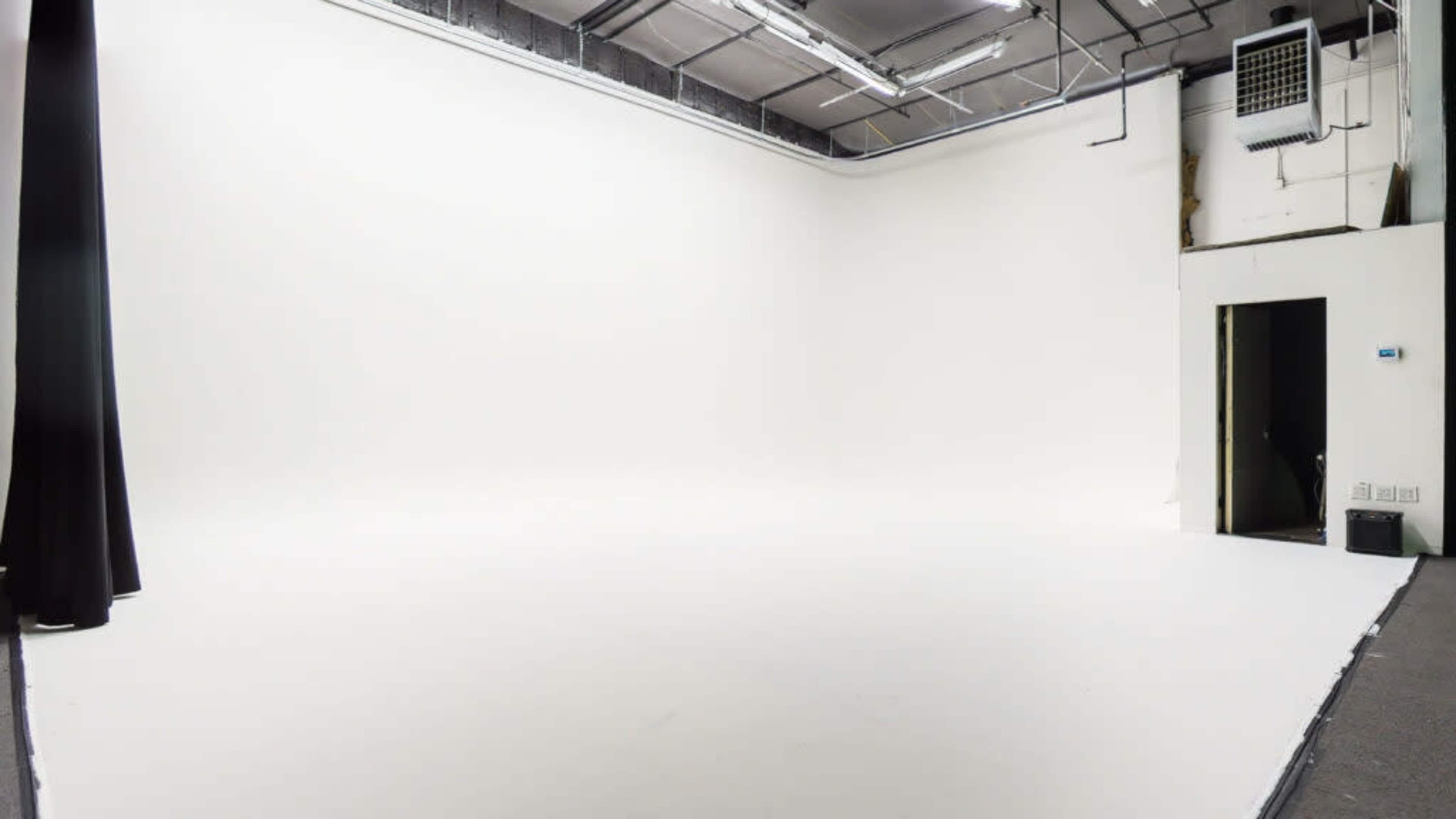 A blank, well-lit studio space with white walls and a smooth floor.