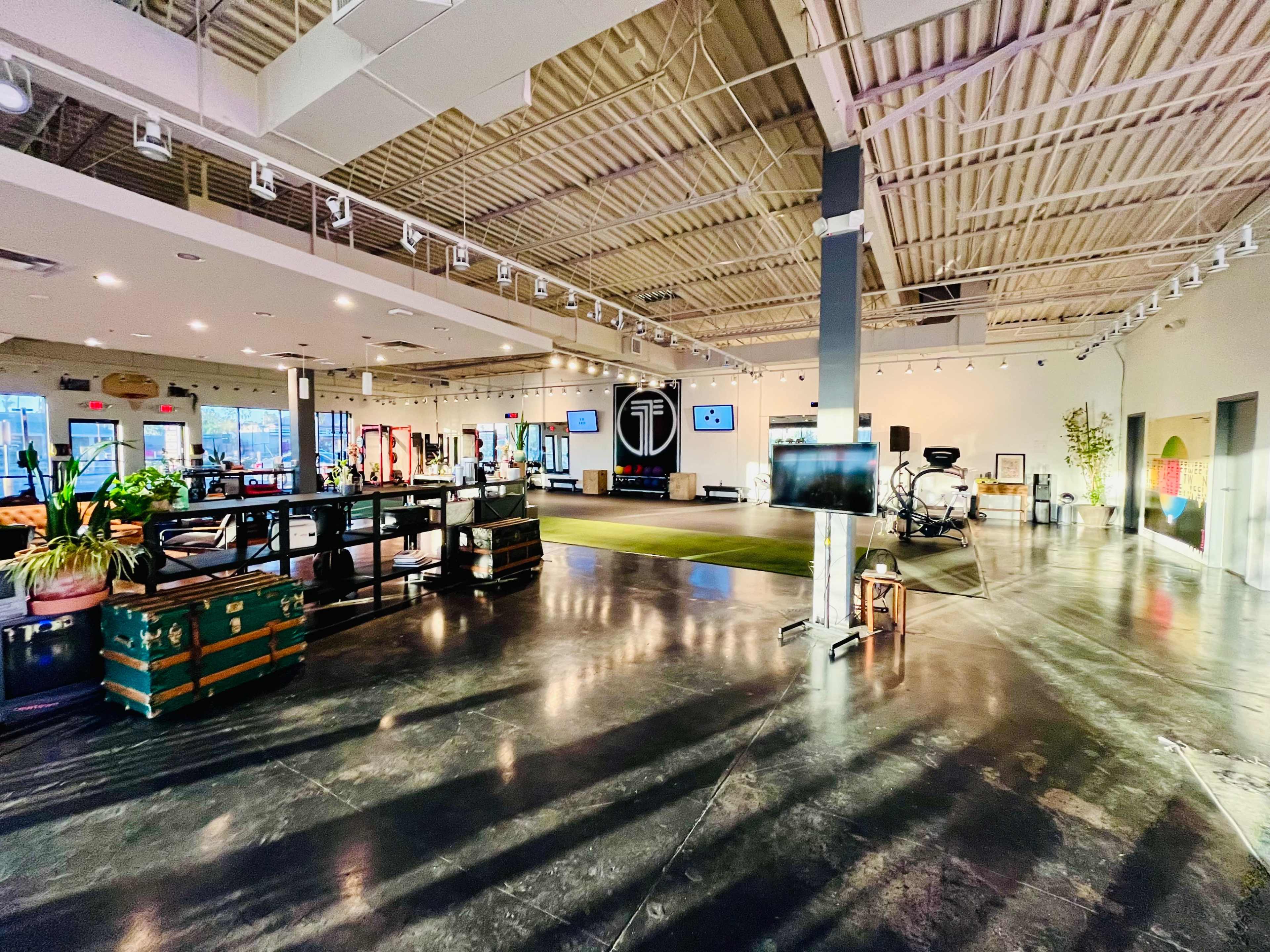 A spacious, well-lit interior of a modern studio with polished concrete floors, various art pieces, and equipment set up for an event or presentation.