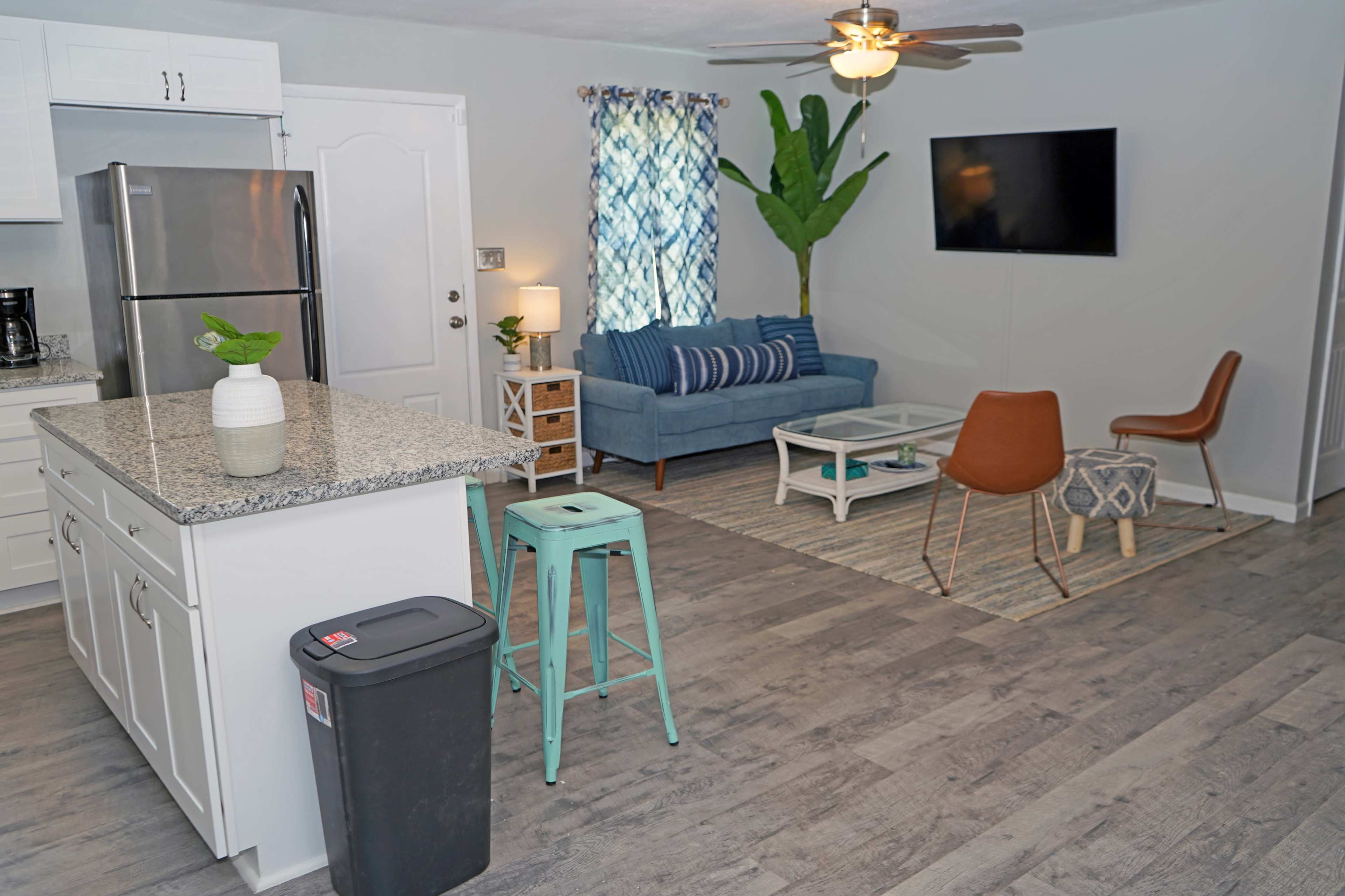 A modern living space with a kitchen island, a blue couch, a coffee table, and a television mounted on the wall.