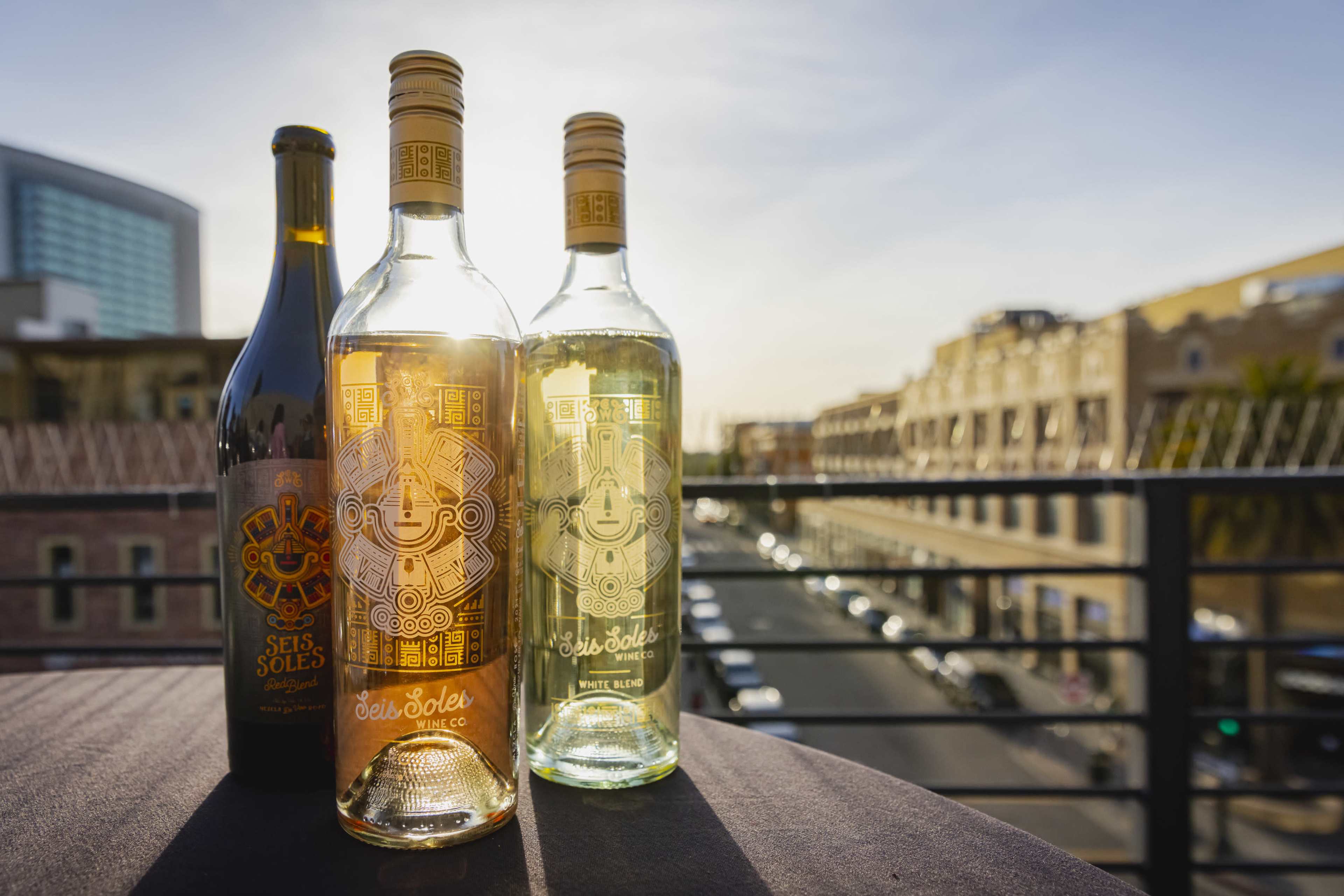 Two bottles of Seis Soles wine, one white and one rosé, are displayed on a table with a city street visible in the background during sunset.