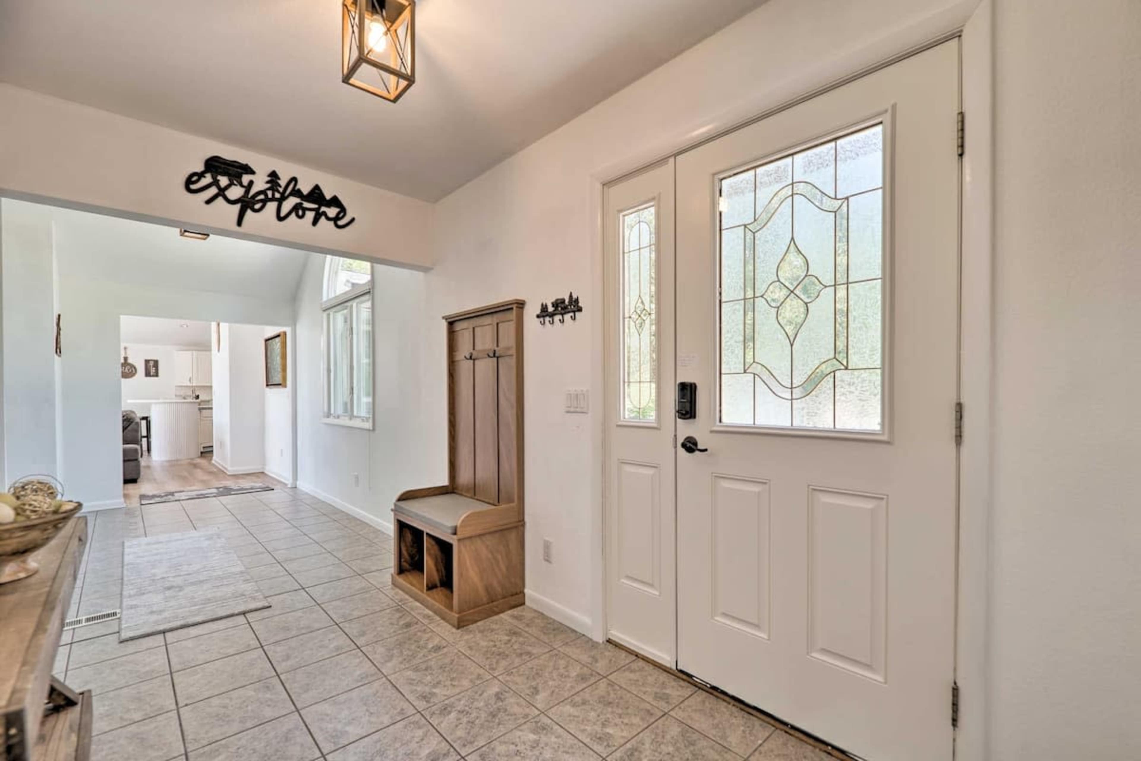 A foyer with a decorative light fixture, a glass-front door, and a bench with hooks on the side.