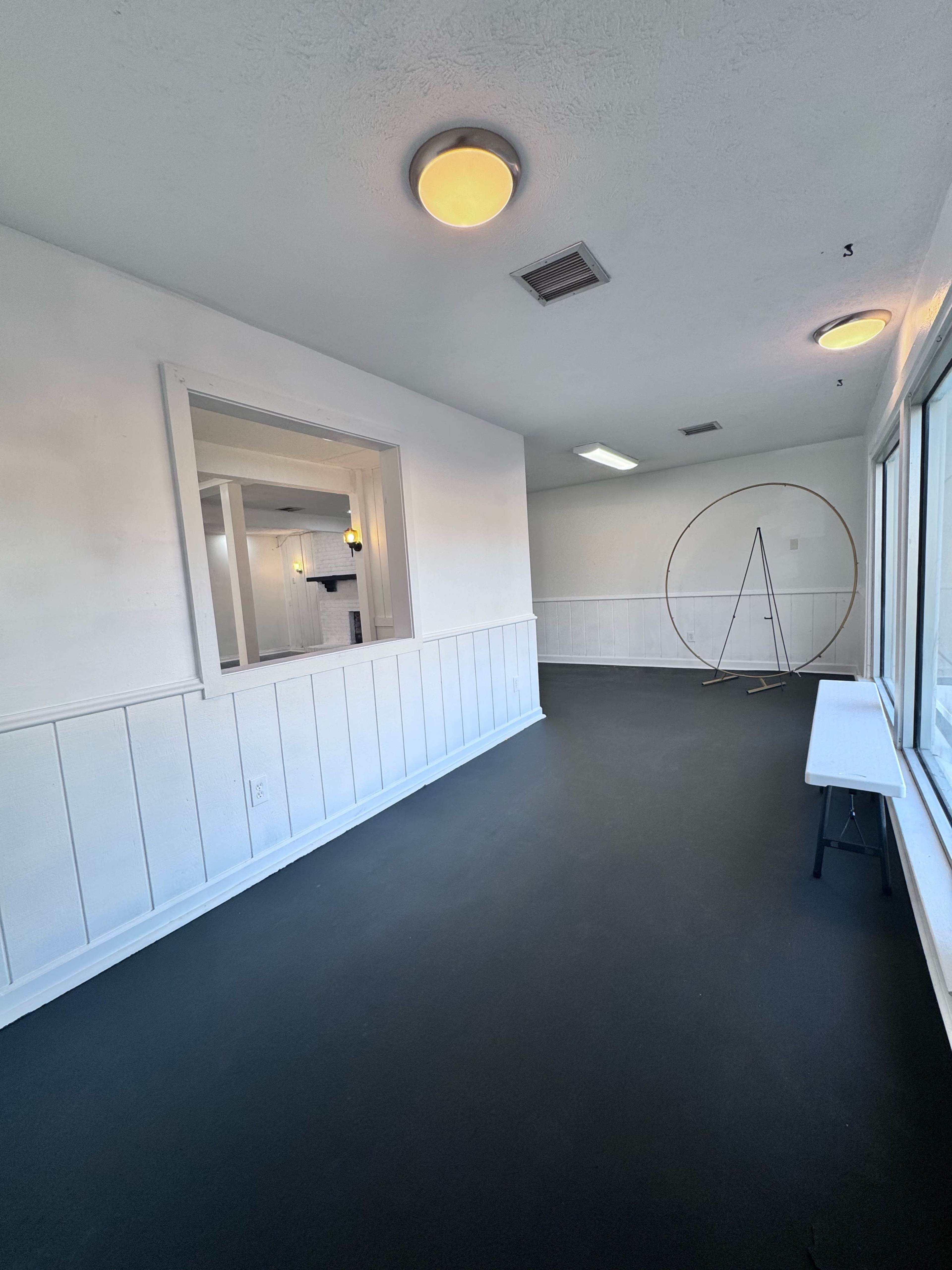 A spacious, minimally furnished room with white walls, a dark floor, and a circular stand in the center.