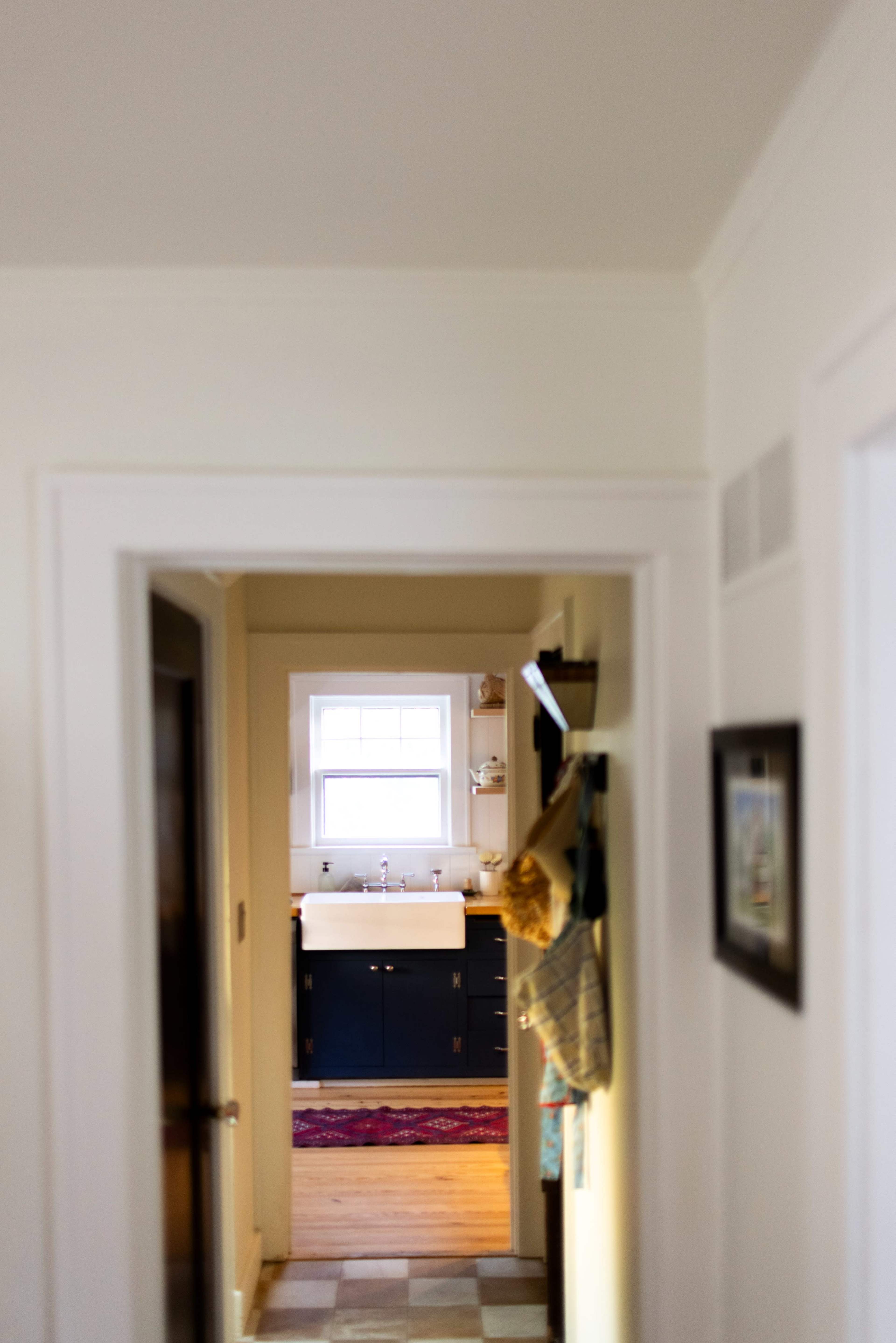 A hallway leads to a brightly lit bathroom featuring a double sink and dark cabinetry.