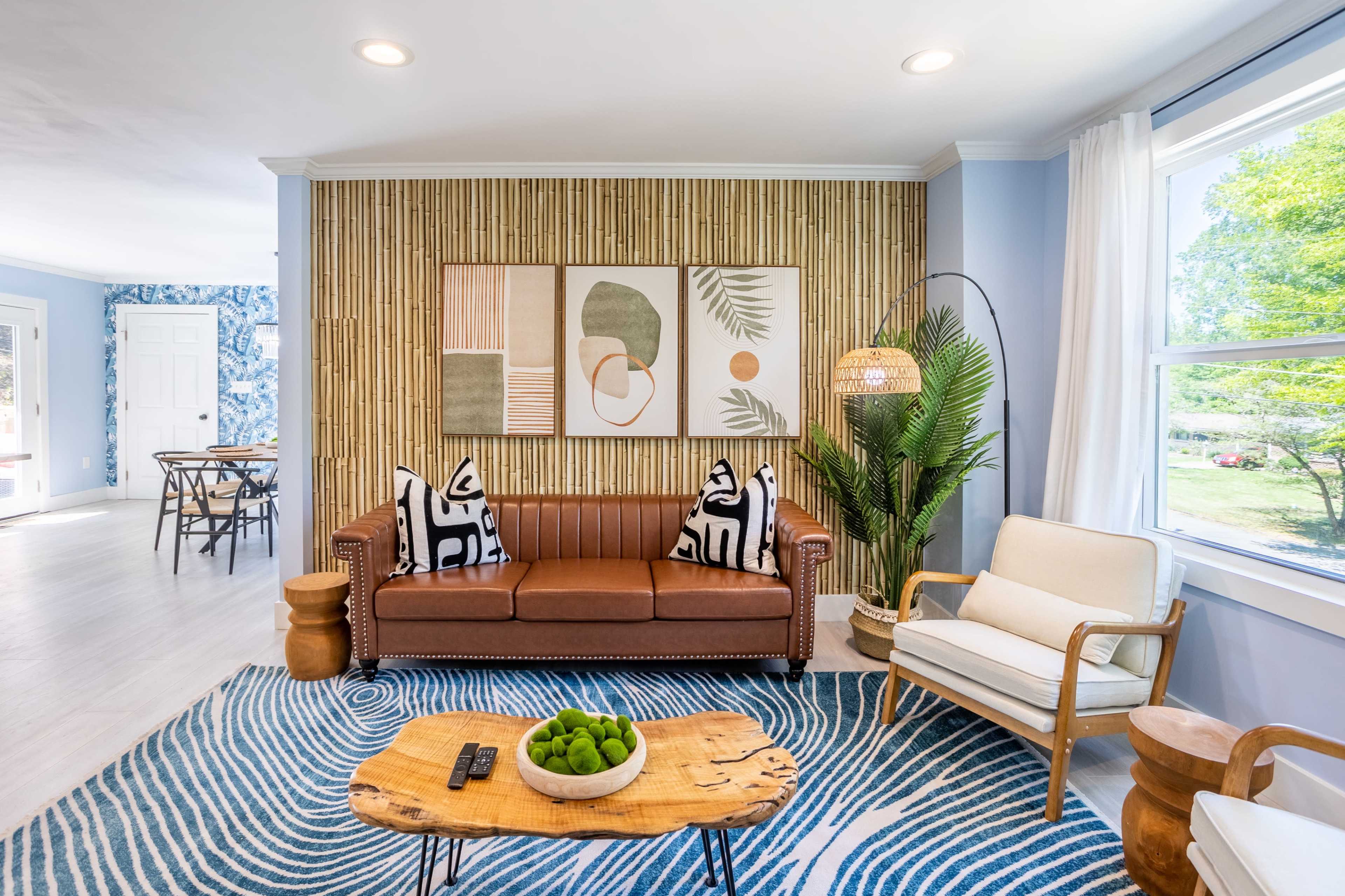 The living room features a brown couch with patterned pillows, a rustic wooden coffee table, and a wall adorned with framed artwork and bamboo accents.