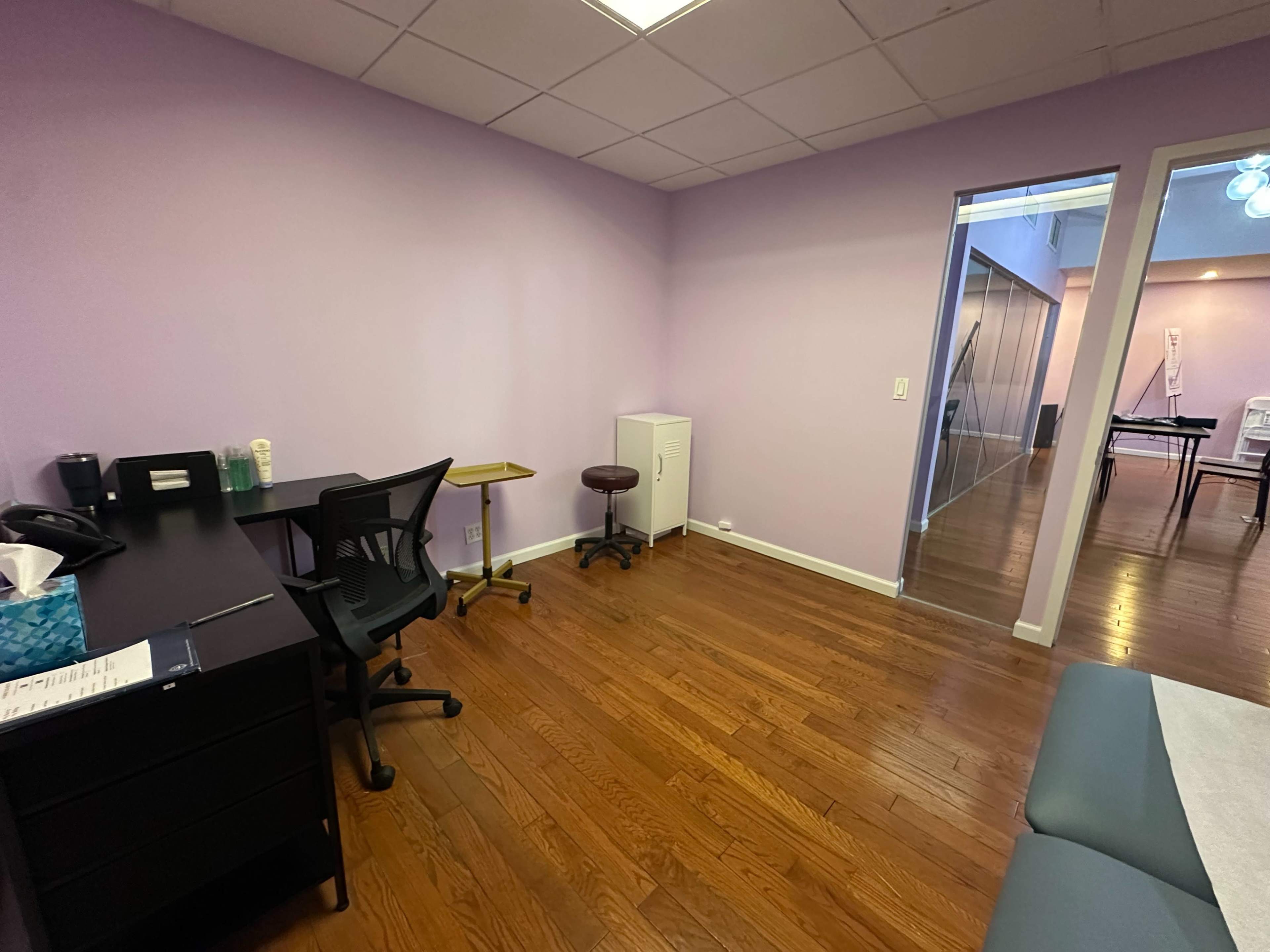 The image shows a small office with purple walls, a desk and chair, a stool, and a white cabinet.