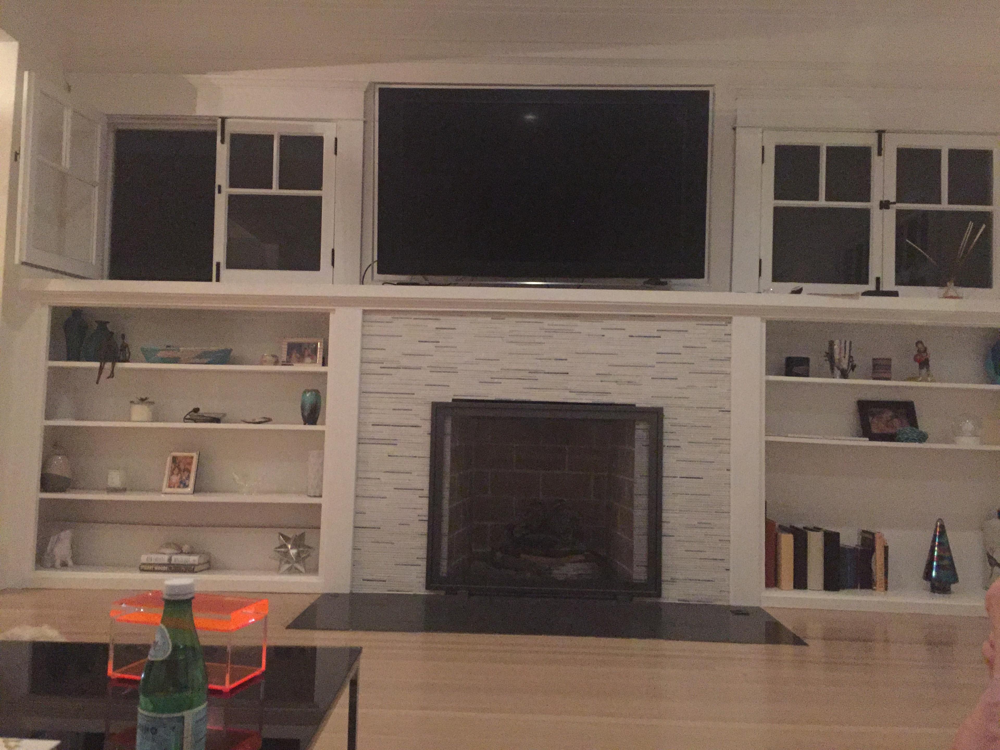A living room with a fireplace, a television mounted above it, and built-in shelves on either side filled with various decorative items.