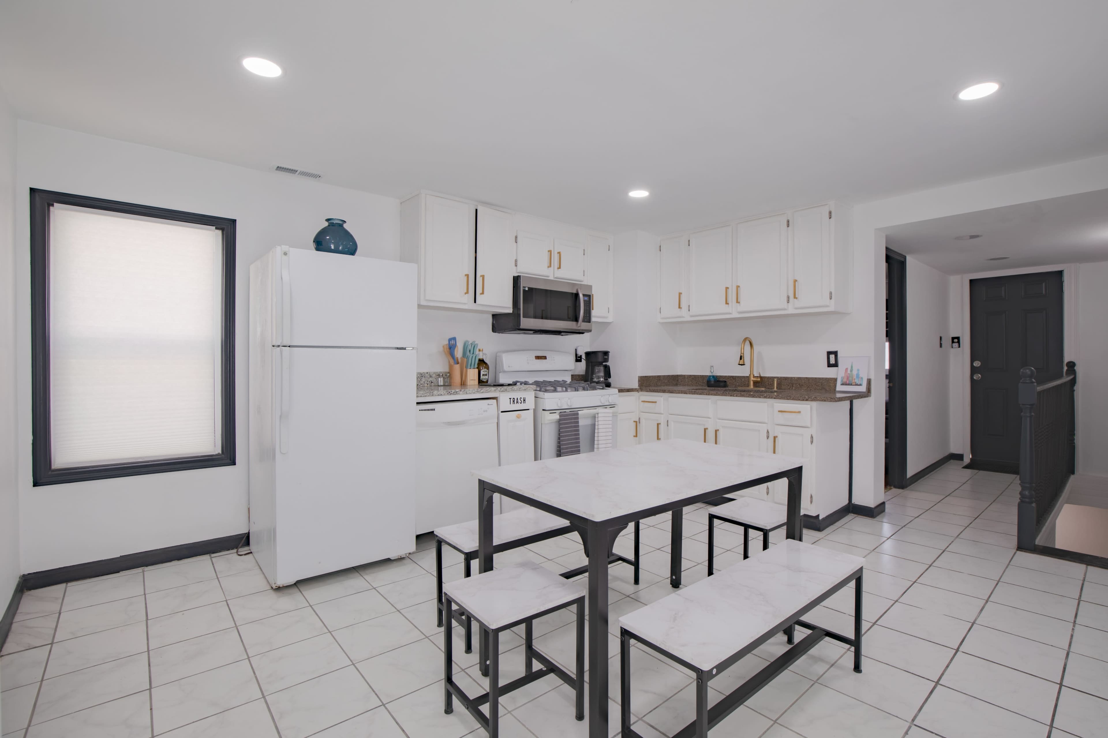 A modern kitchen with white cabinets, stainless steel appliances, and a gray dining table with benches.
