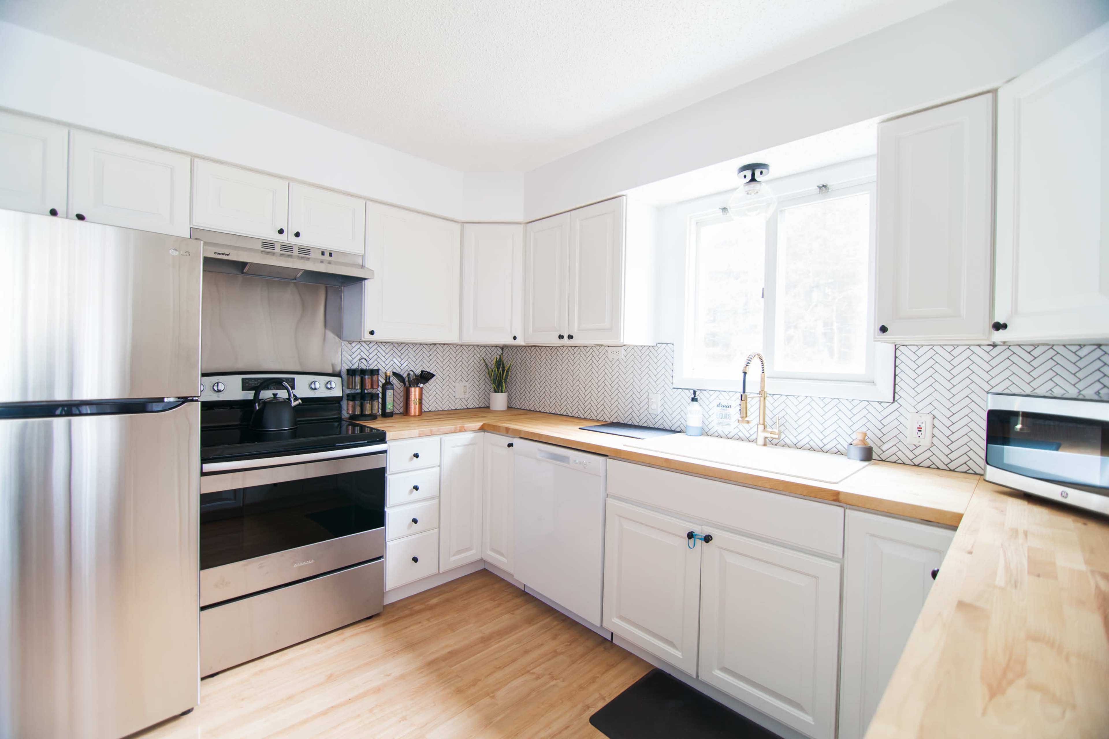 The kitchen features white cabinetry, stainless steel appliances, and a wooden countertop with a window above the sink.