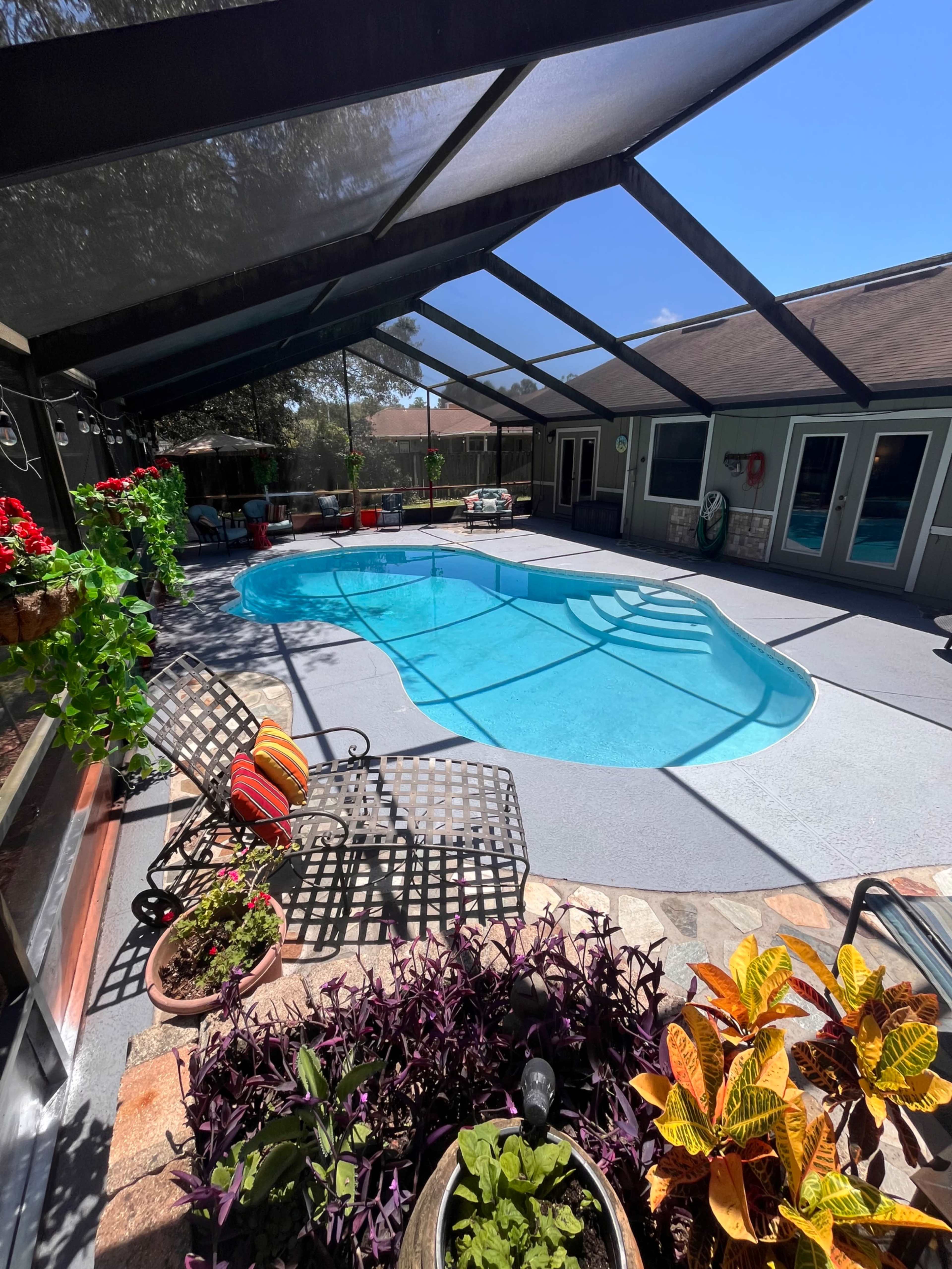 A clear swimming pool is surrounded by a screened patio, with potted plants and outdoor furniture positioned nearby.