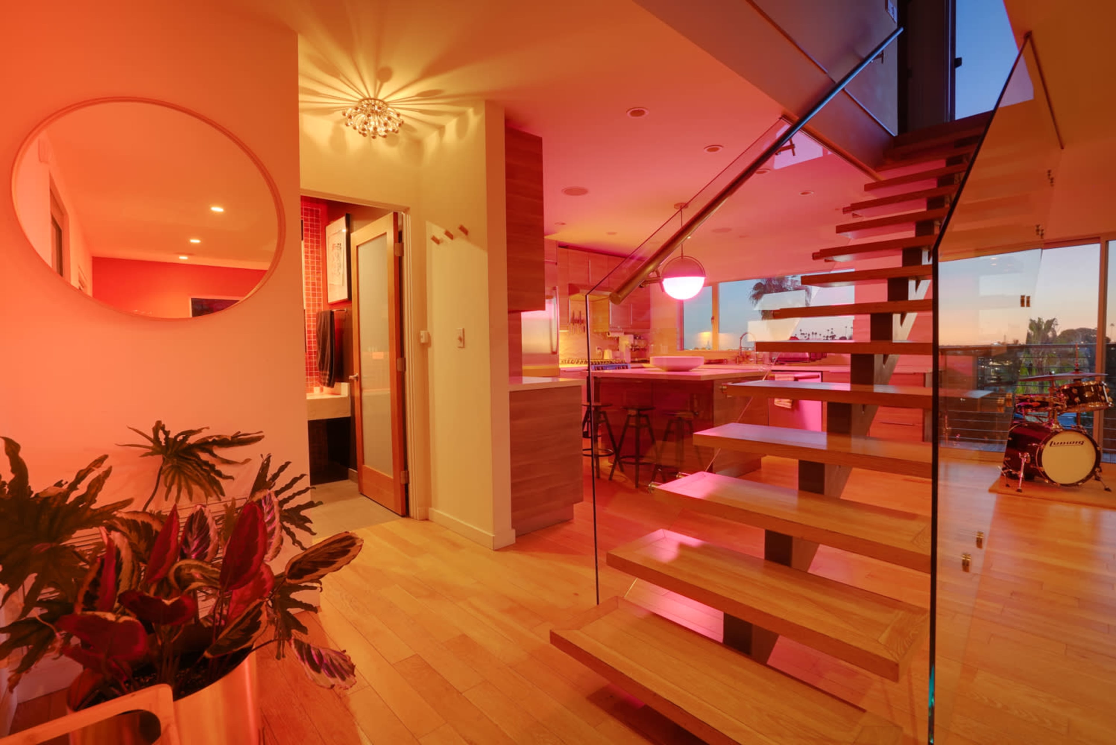 A modern interior space with a wooden staircase leading to an upper level, illuminated by soft lighting and featuring a large window with a view.