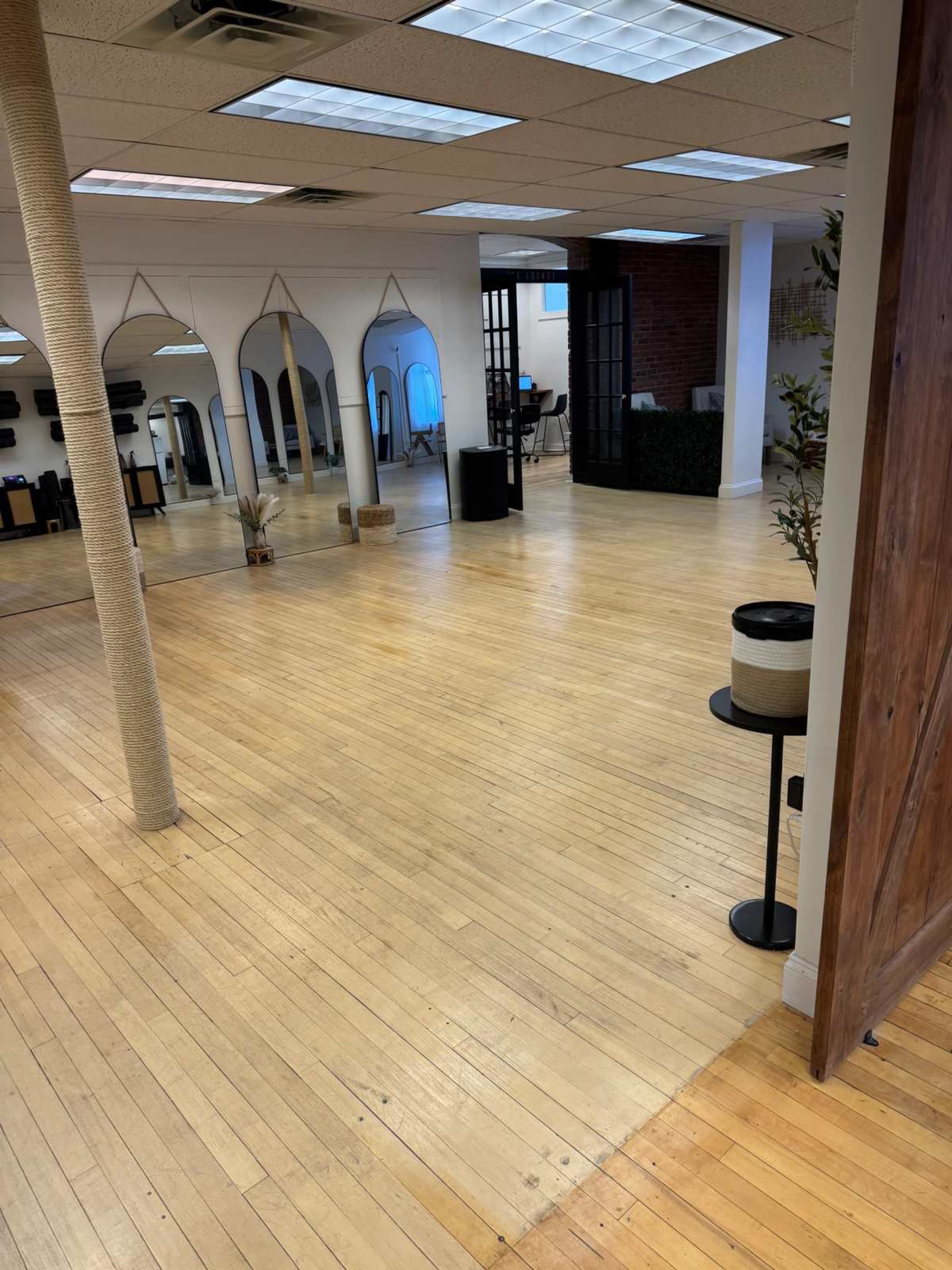 The image shows a spacious, well-lit interior of an office or studio with wooden floors, archways, and various decorative elements.