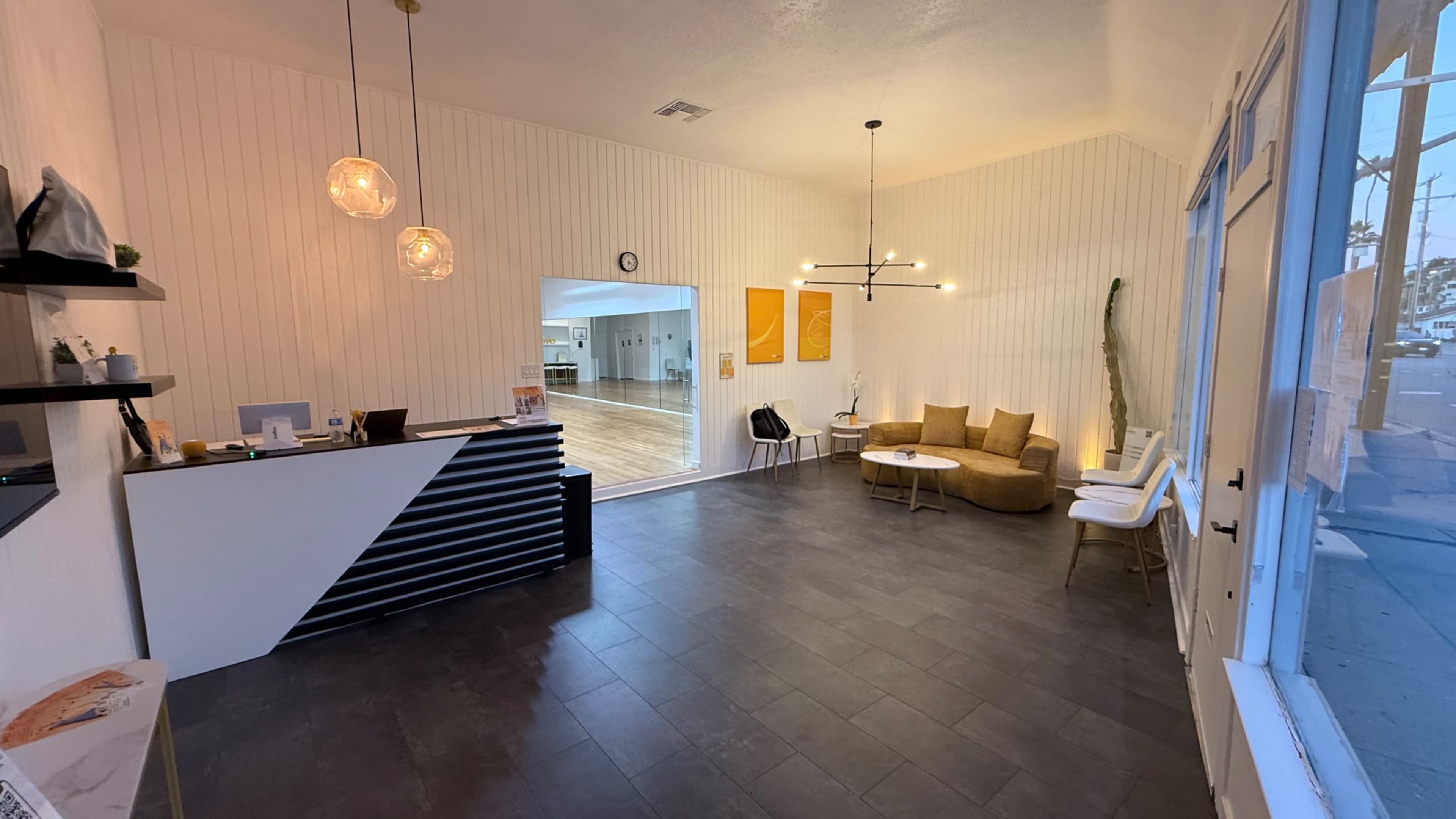 The image shows a modern reception area with a sleek front desk, a seating arrangement of a curved couch and chairs, and a spacious room leading to another area through an archway.