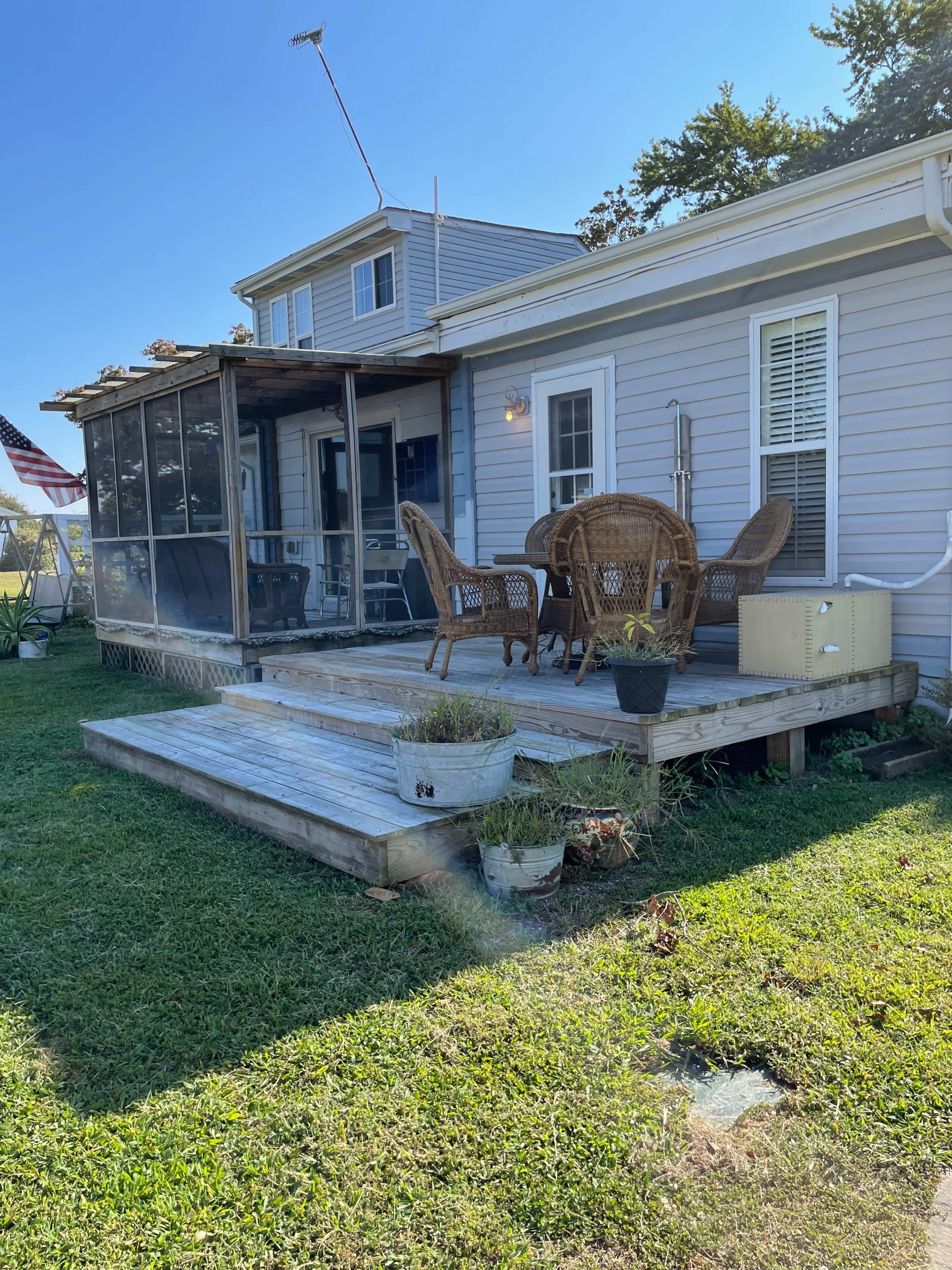 A wooden deck with outdoor seating and a screened porch attached to a gray house, surrounded by grassy areas.