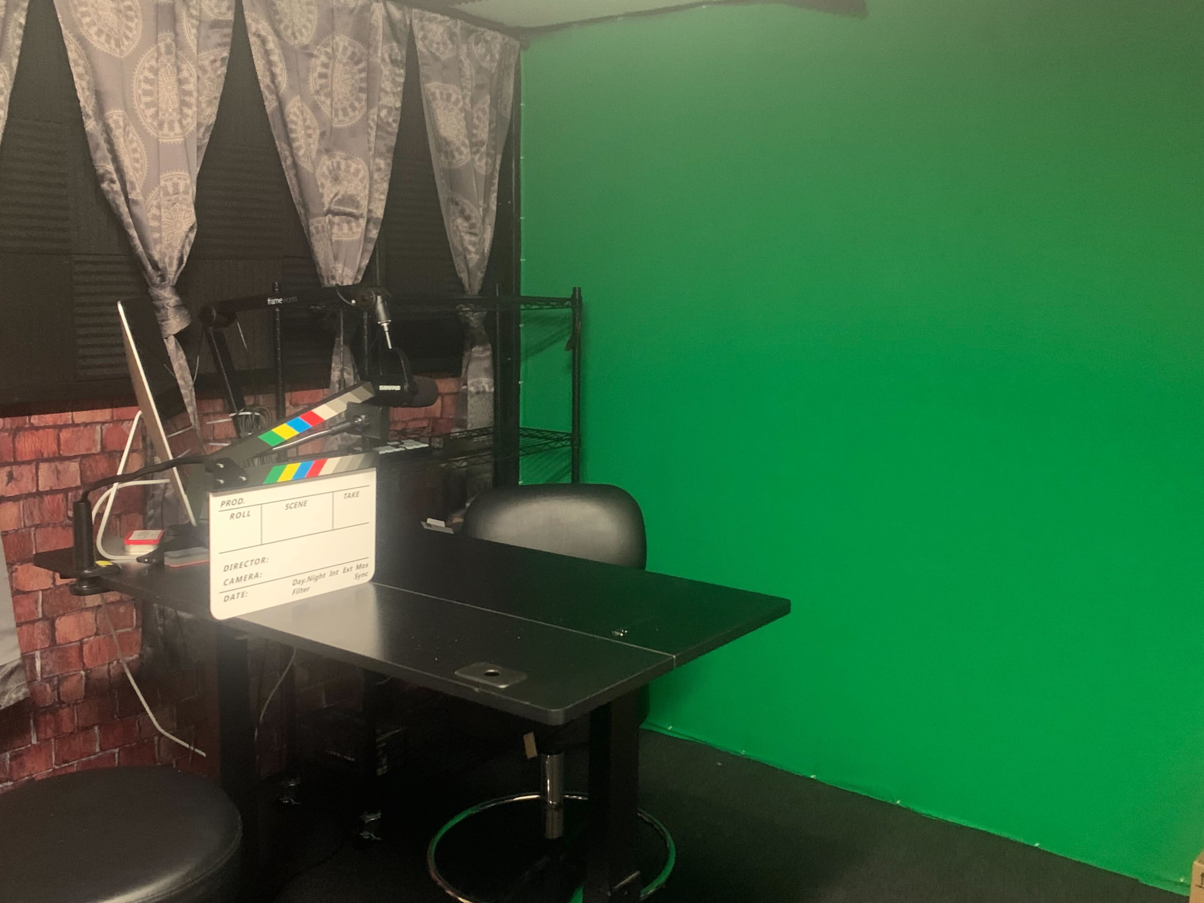 A small room with a green screen wall, a desk with a film clapperboard, and a chair.