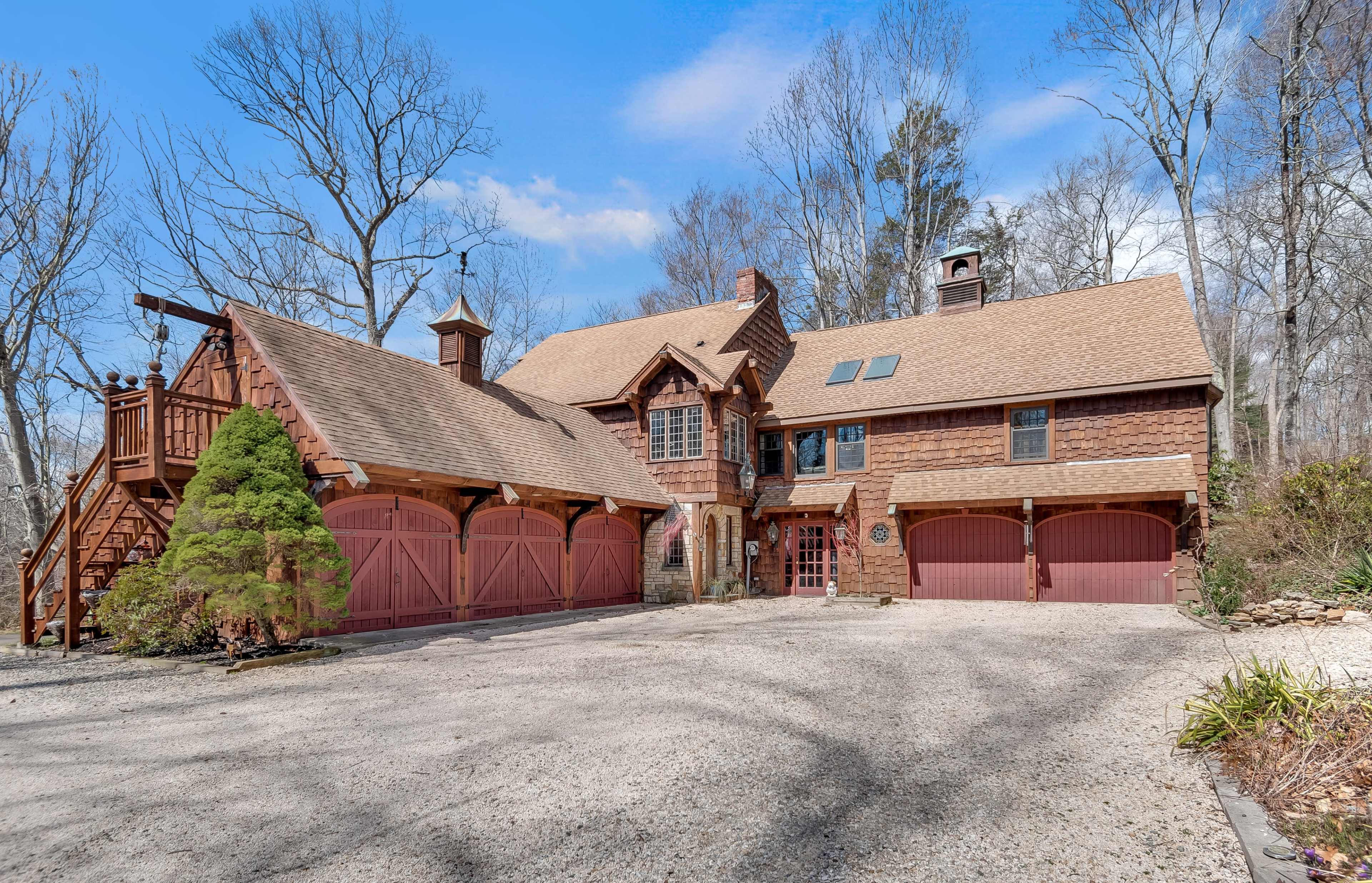 A large, rustic-style home with a gravel driveway and red garage doors is surrounded by bare trees.