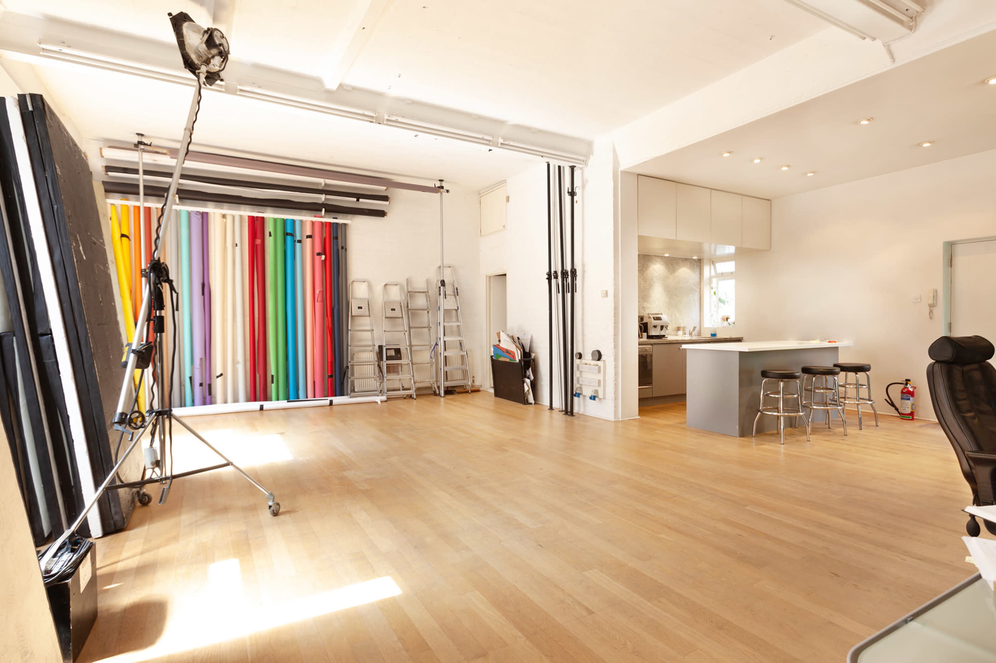 A spacious photography studio with colorful backdrops on one wall and a modern kitchen area in the background.