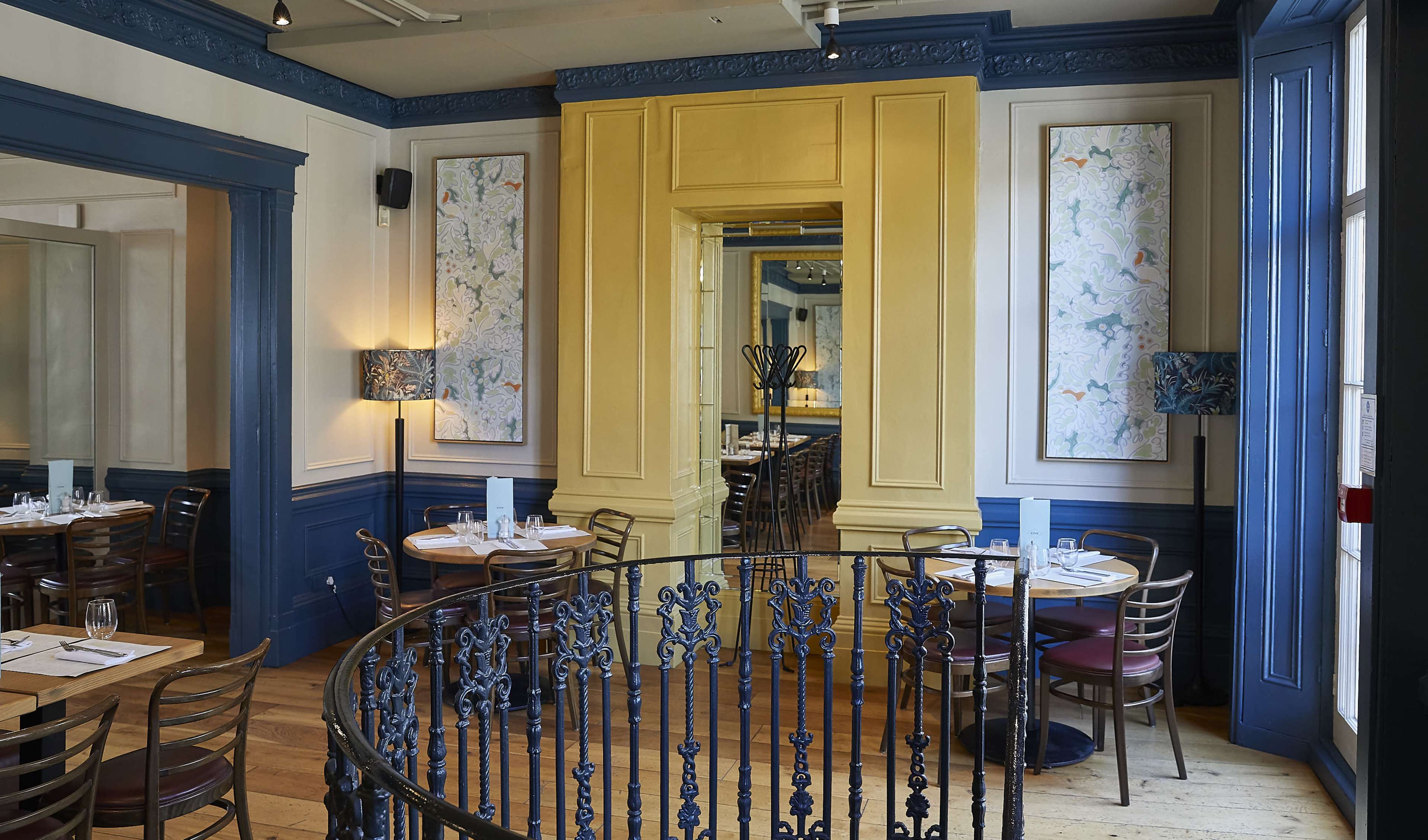 The image shows a brightly lit restaurant interior featuring blue and yellow walls, wooden furniture, and decorative artwork.