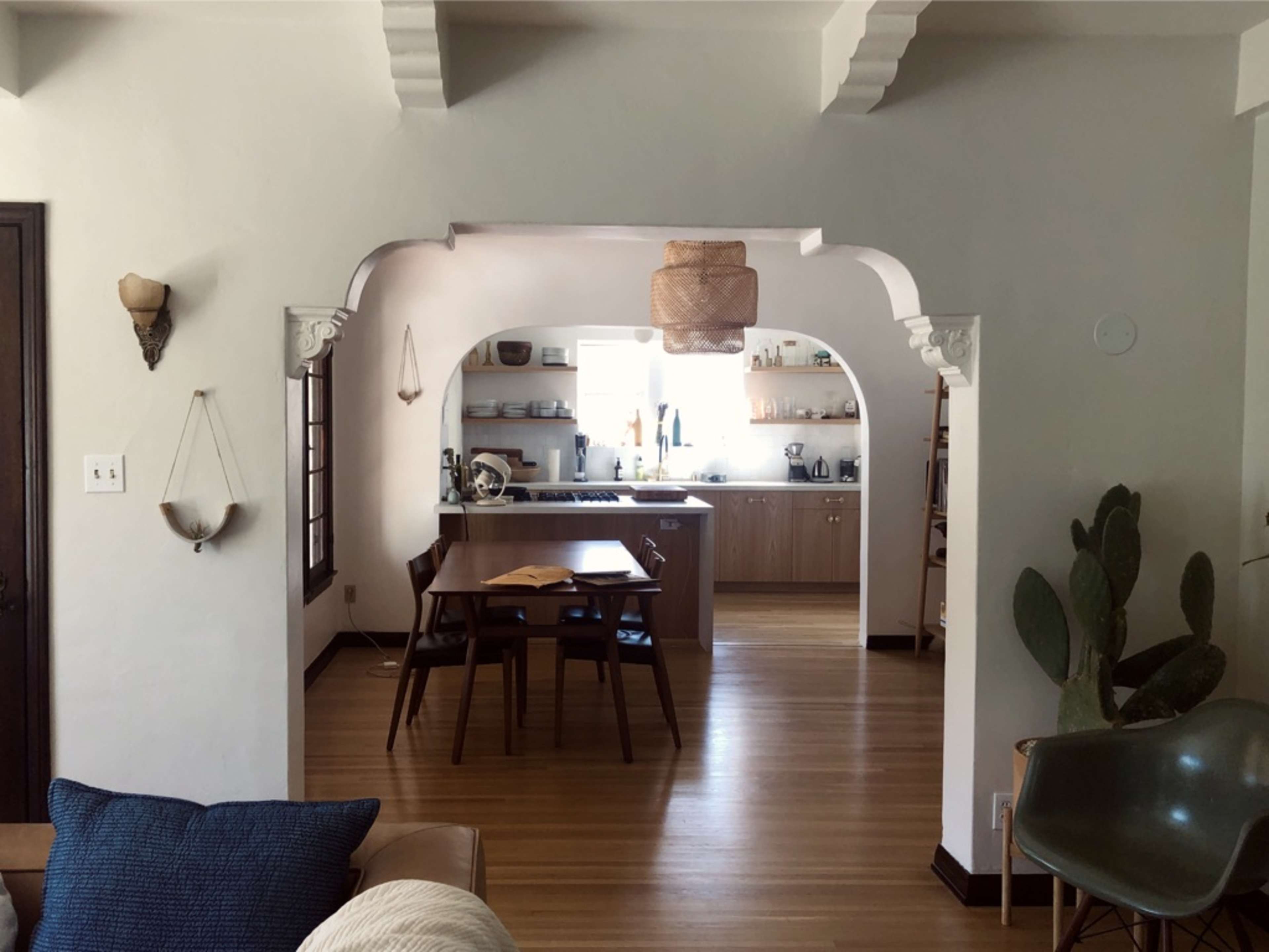 A bright, open living space with a dining table, kitchen, and decorative elements like a cactus and light fixtures.