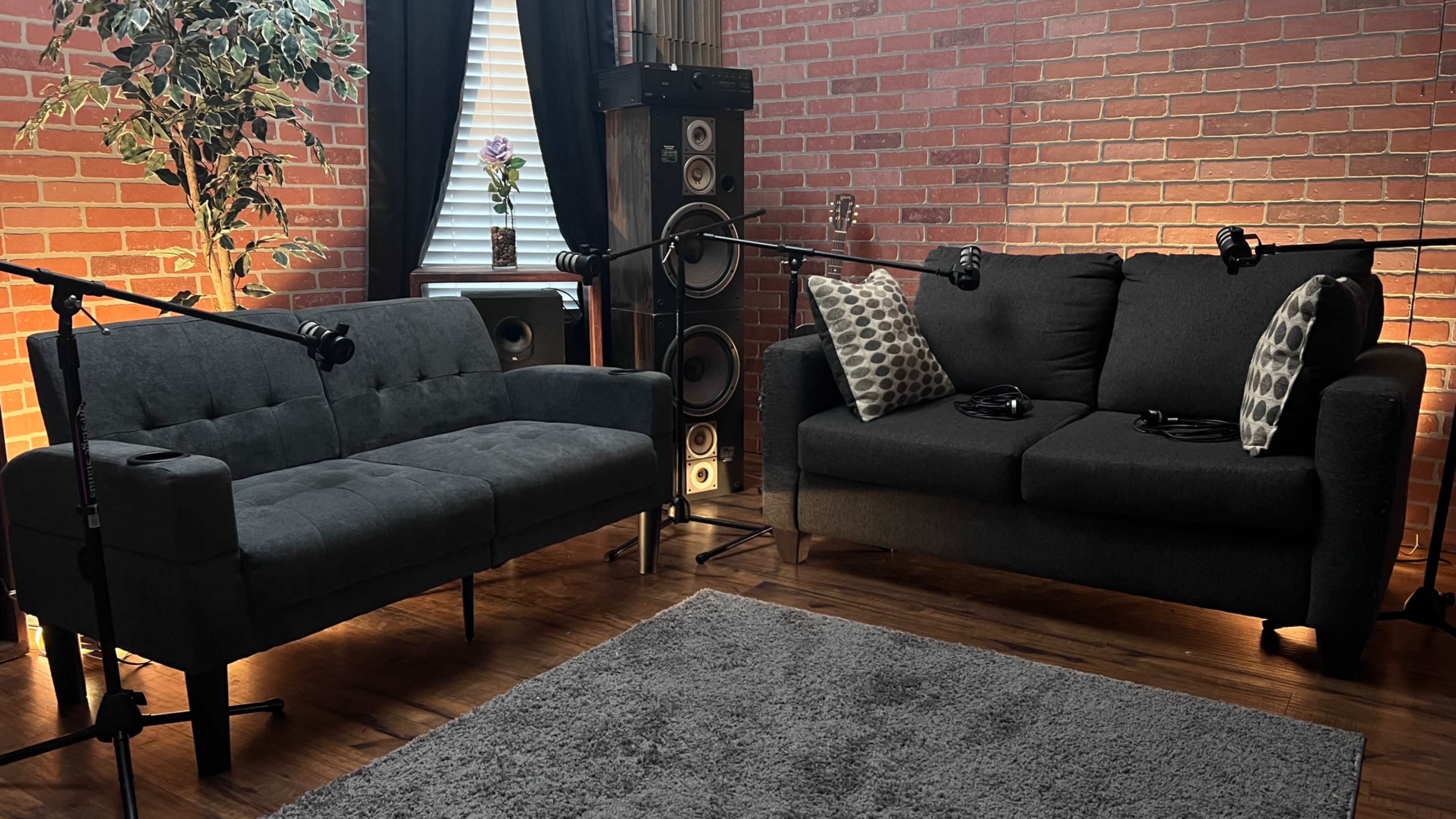 A cozy living room with two dark gray sofas, a rug, and audio equipment, illuminated by soft lighting.