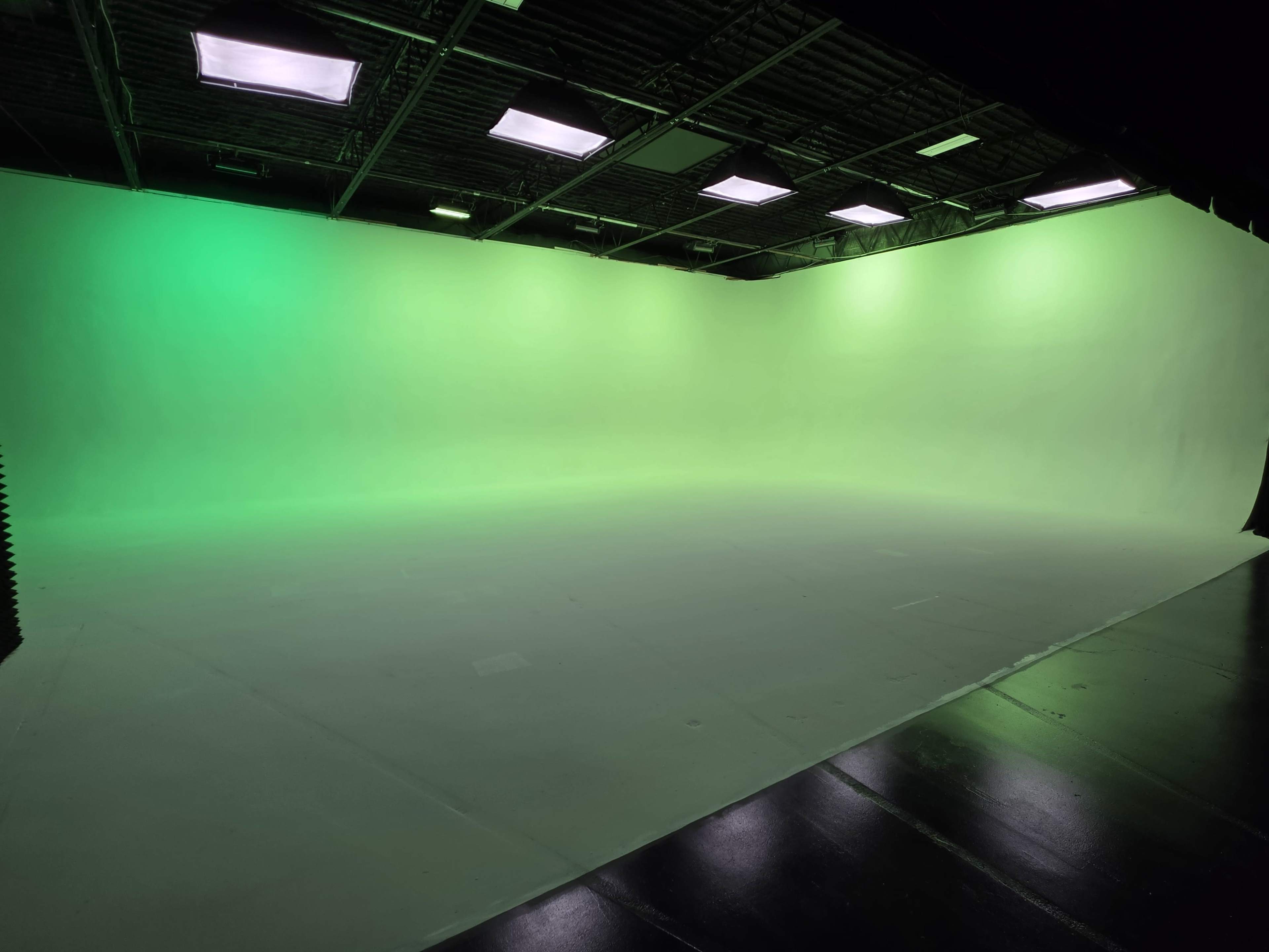The image shows a spacious studio with a green backdrop and bright overhead lights.