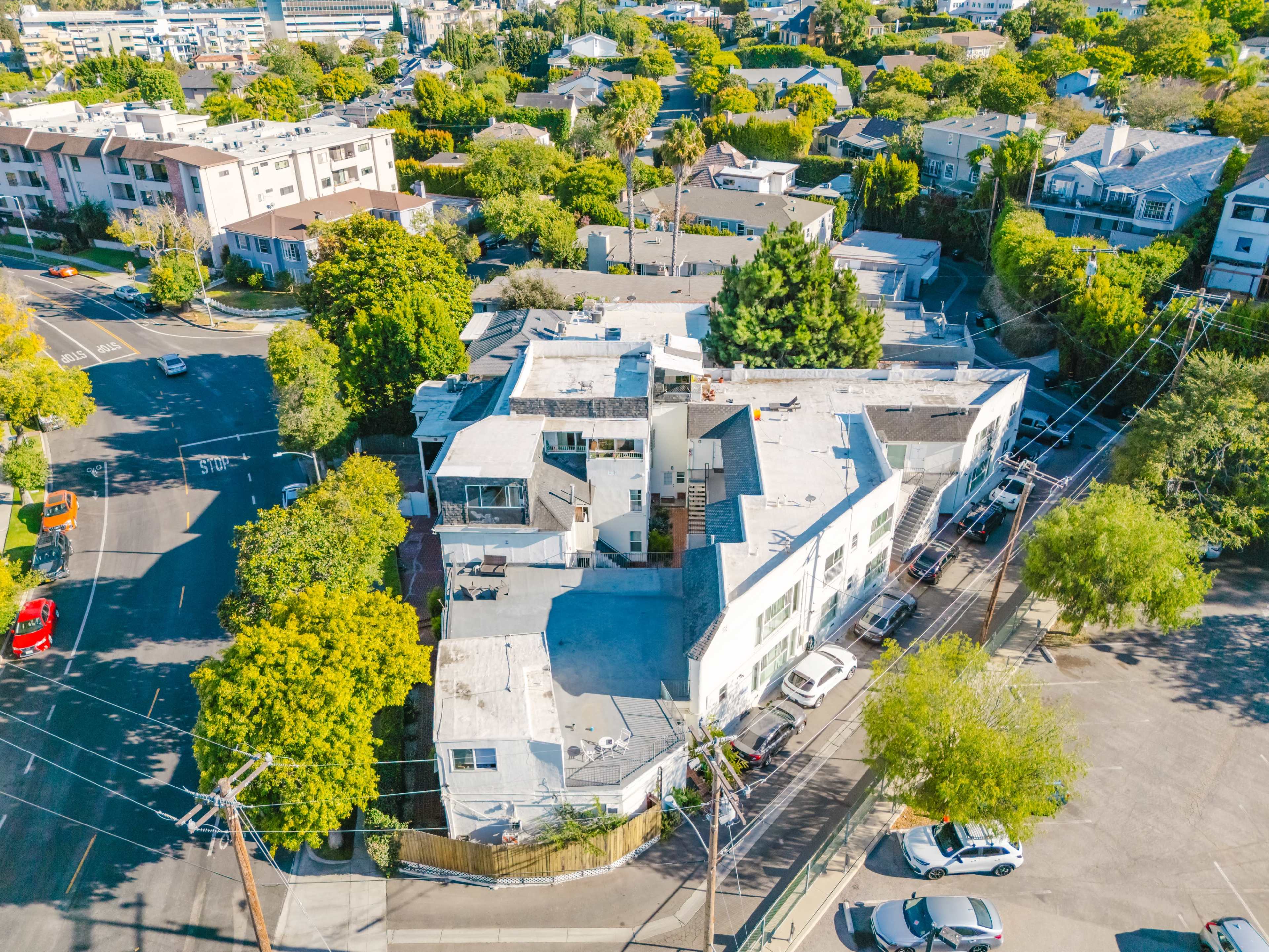 The image shows a multi-level building surrounded by lush greenery and residential homes, located at a street intersection.