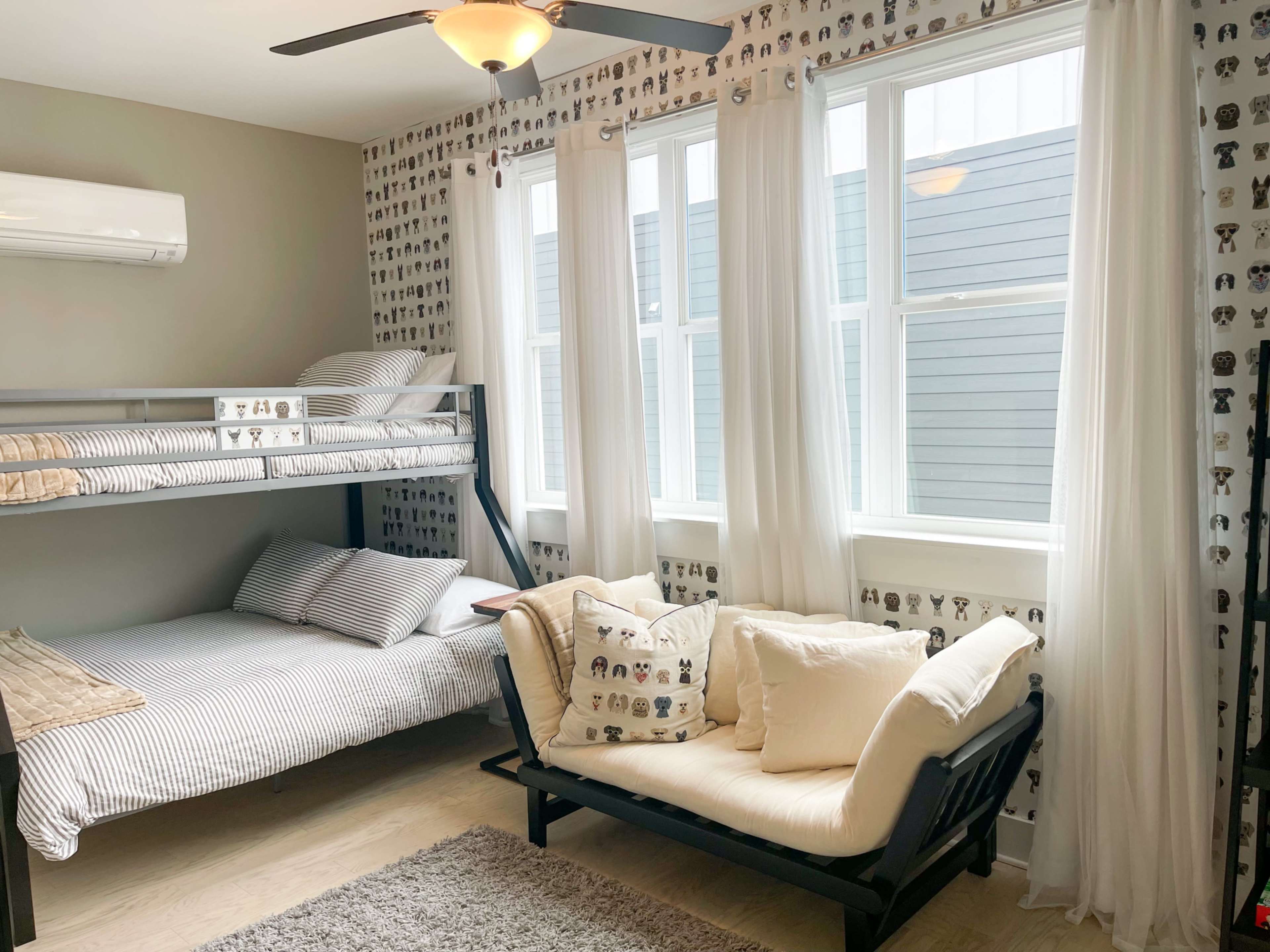 The room features a bunk bed on one side and a seating area with a daybed on the other, with large windows illuminating the space.