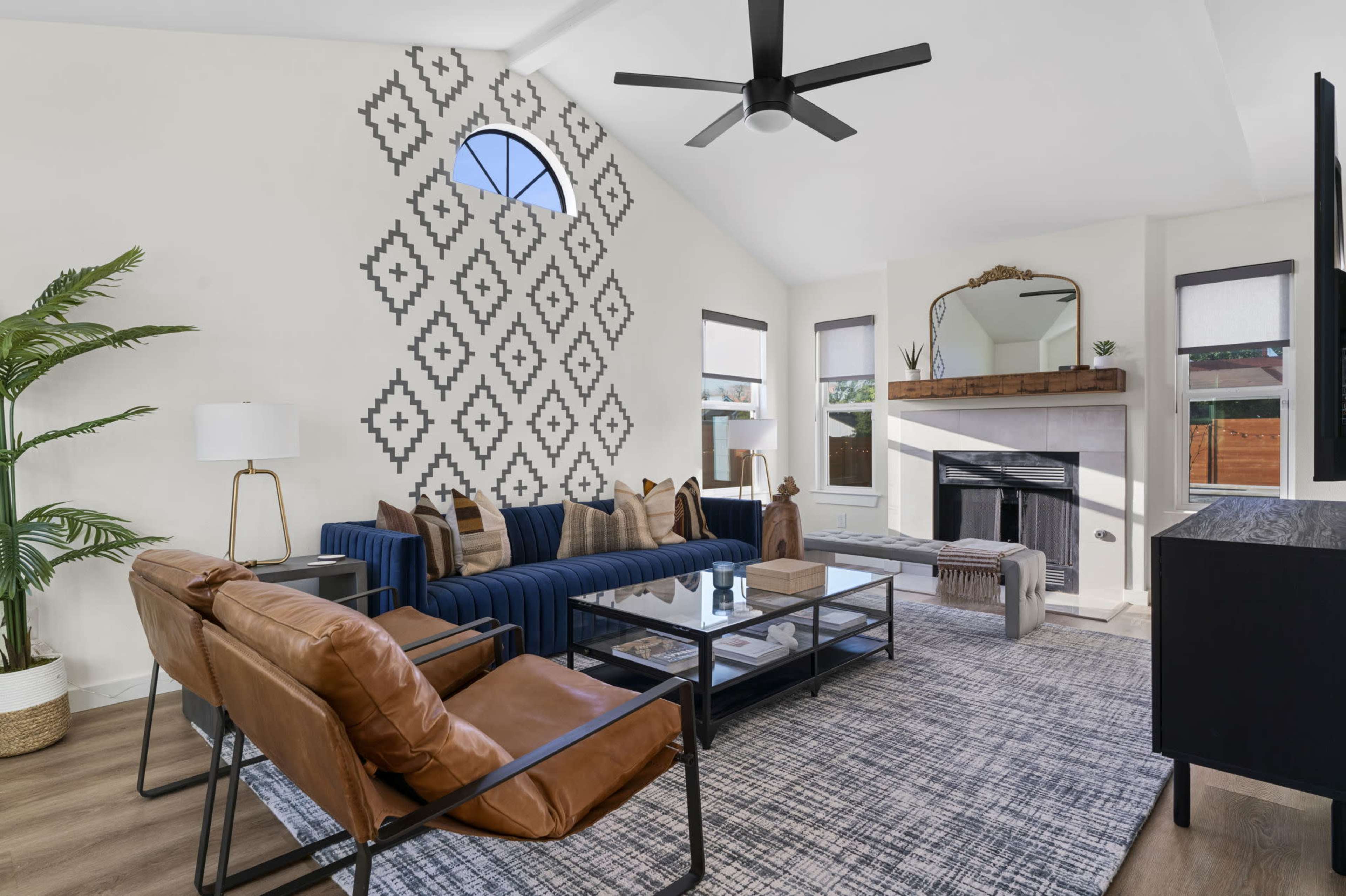 The image features a modern living room with a blue sofa, a leather chair, and a decorative wall pattern, complemented by natural light from large windows.