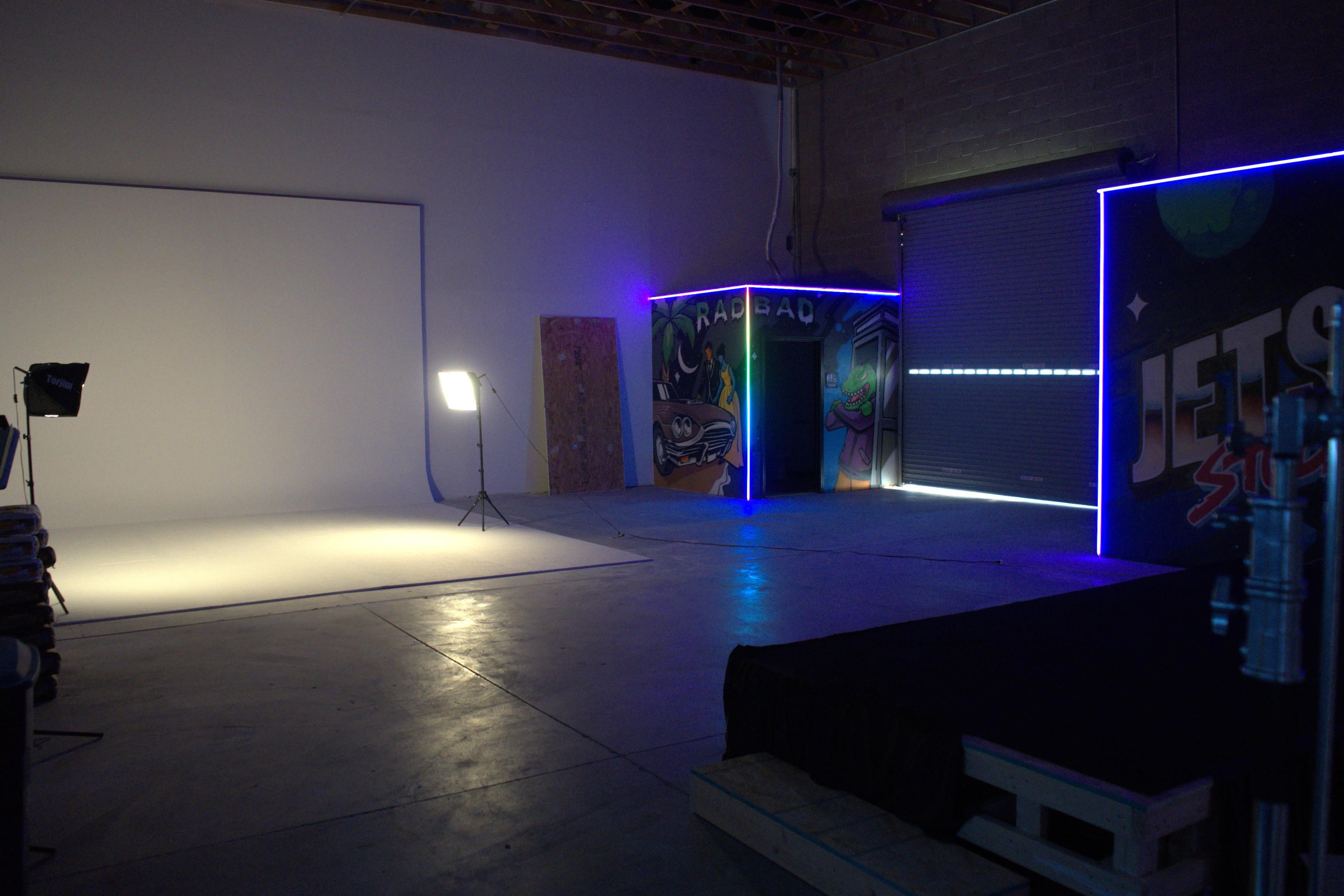 The image shows a studio space with a brightly lit backdrop, an illuminated section featuring colorful graffiti, and a backdrop stand on one side.