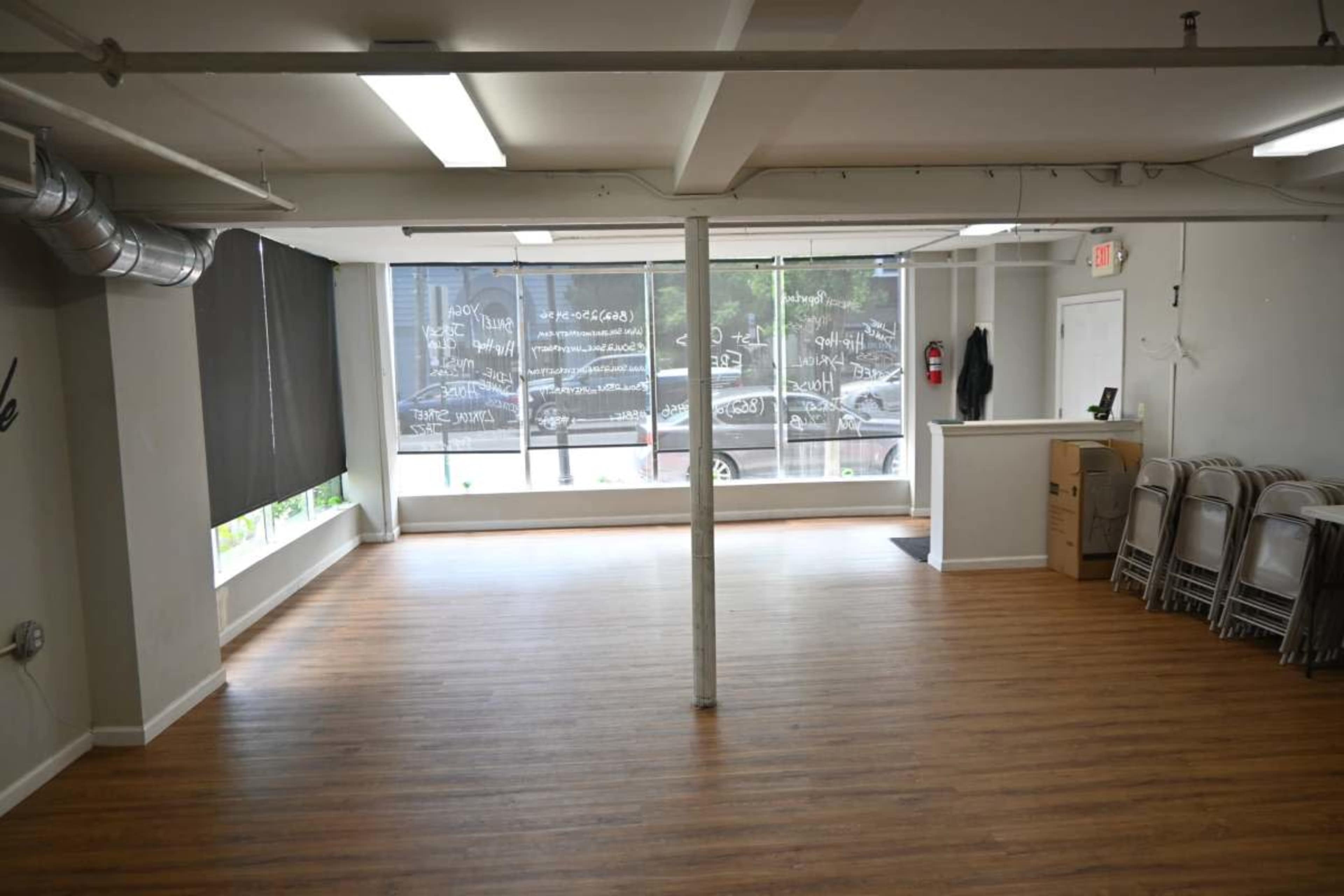 A vacant interior space with wooden flooring, large windows, and a reception area at one end.