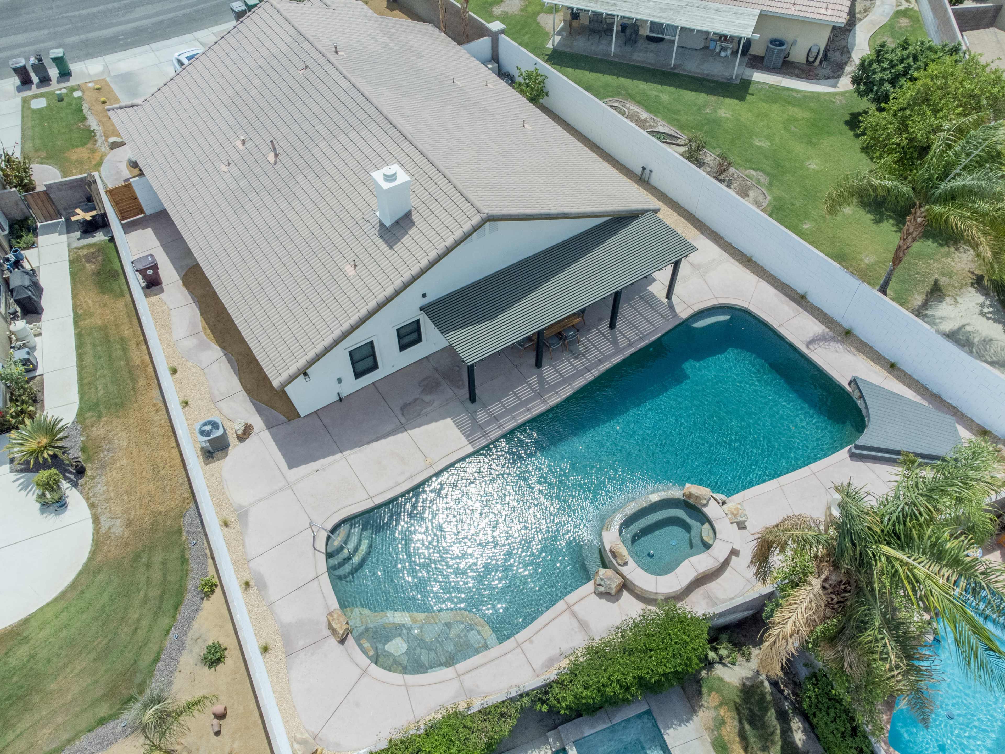 An aerial view shows a house with a pool and spa in the backyard, surrounded by a fence and landscaped areas.