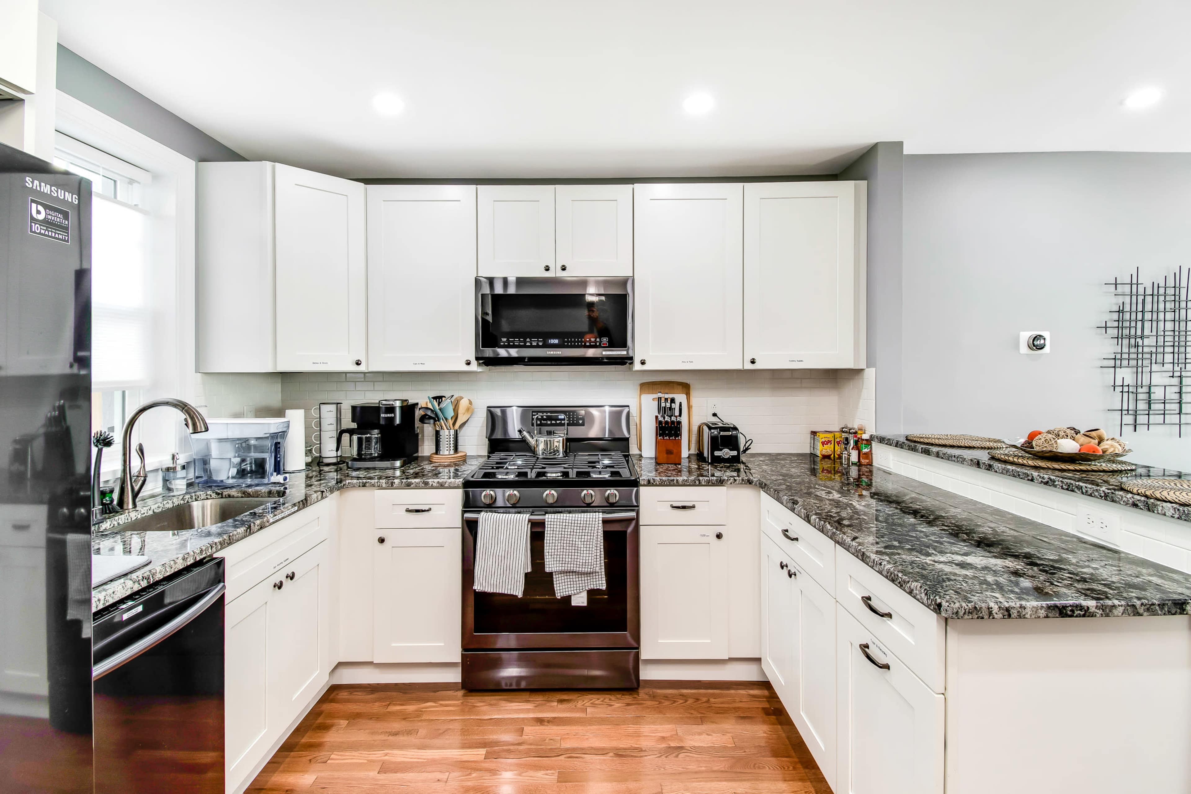 The kitchen features modern white cabinetry, a stainless steel stove, and a granite countertop, with a wooden floor.