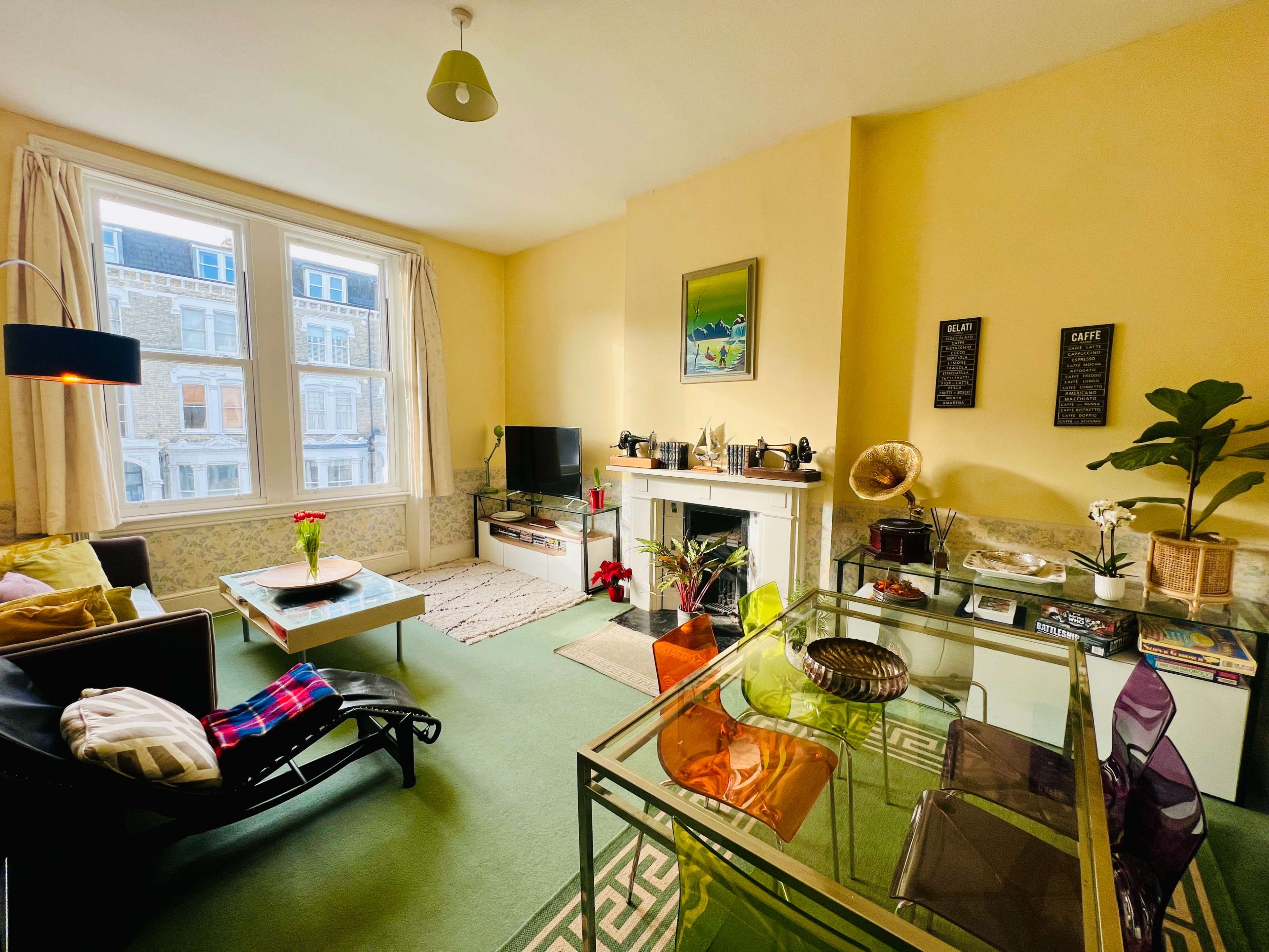 The room features a cozy living area with a television, a glass coffee table, a decorative fireplace, and large windows allowing natural light.