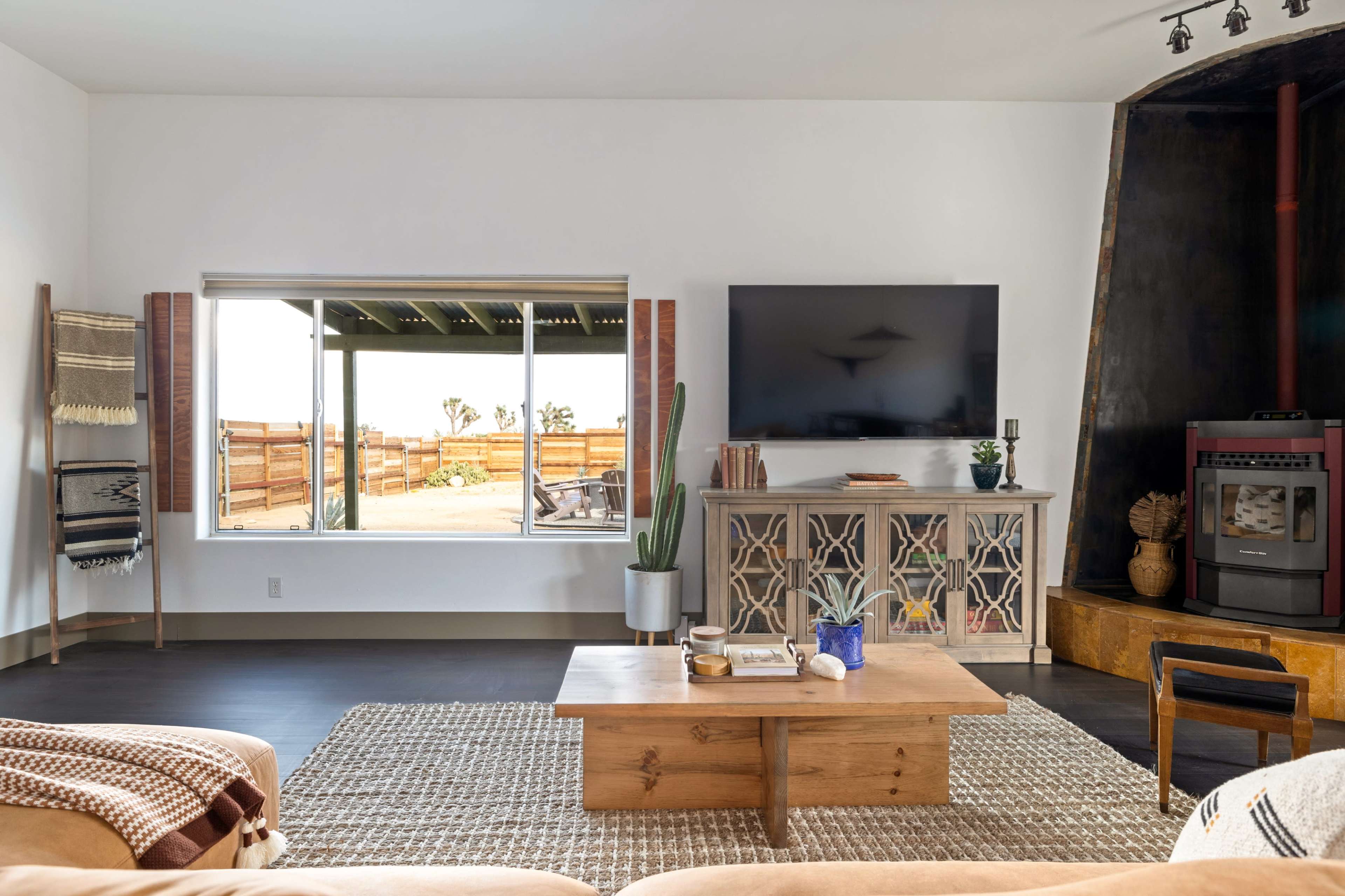 A modern living room features a coffee table, a flat-screen TV mounted on the wall, and large windows displaying an outdoor view.