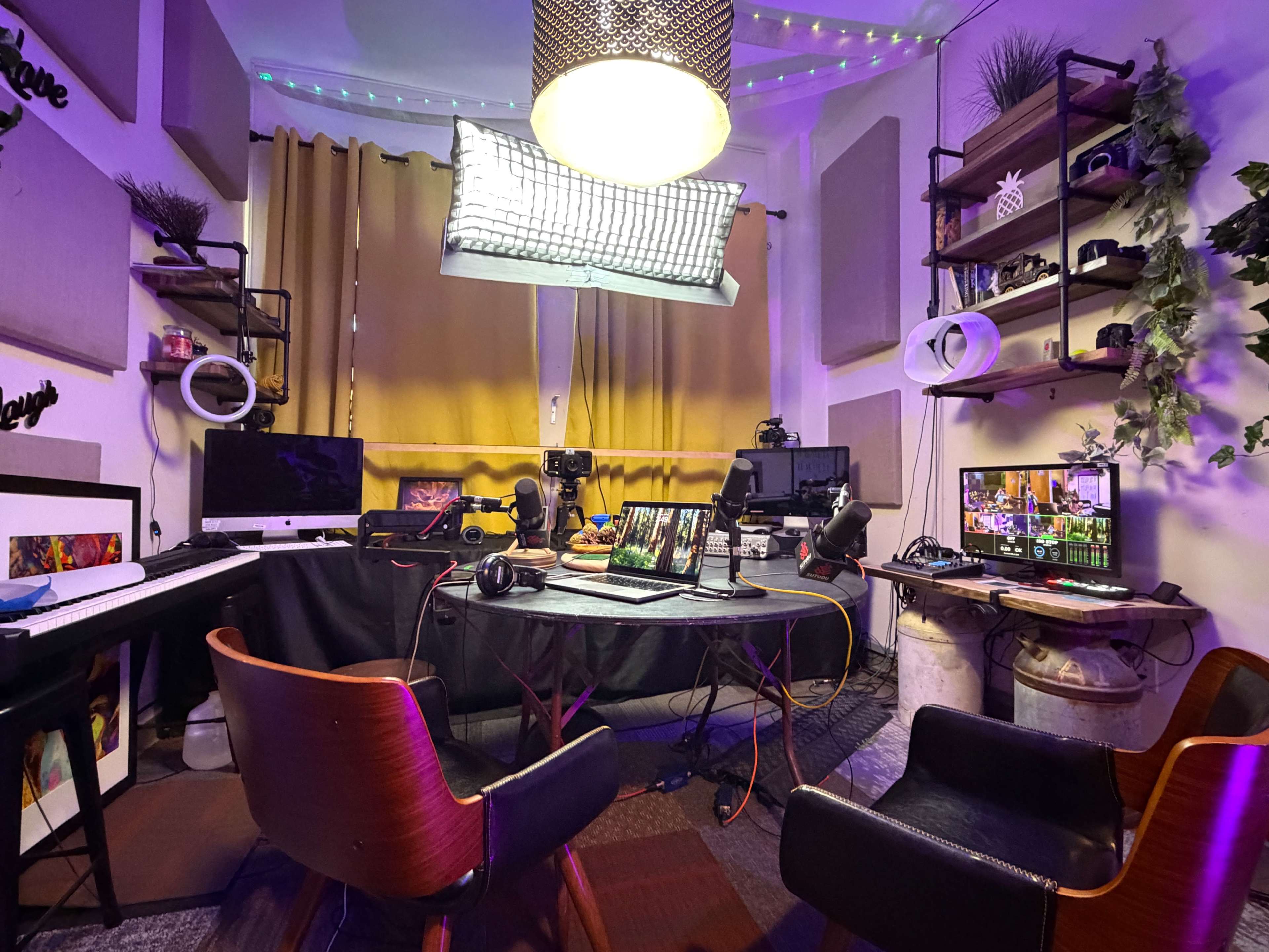 The image shows a recording studio or workspace featuring multiple monitors, microphones, and a keyboard, surrounded by chairs and decorative elements.