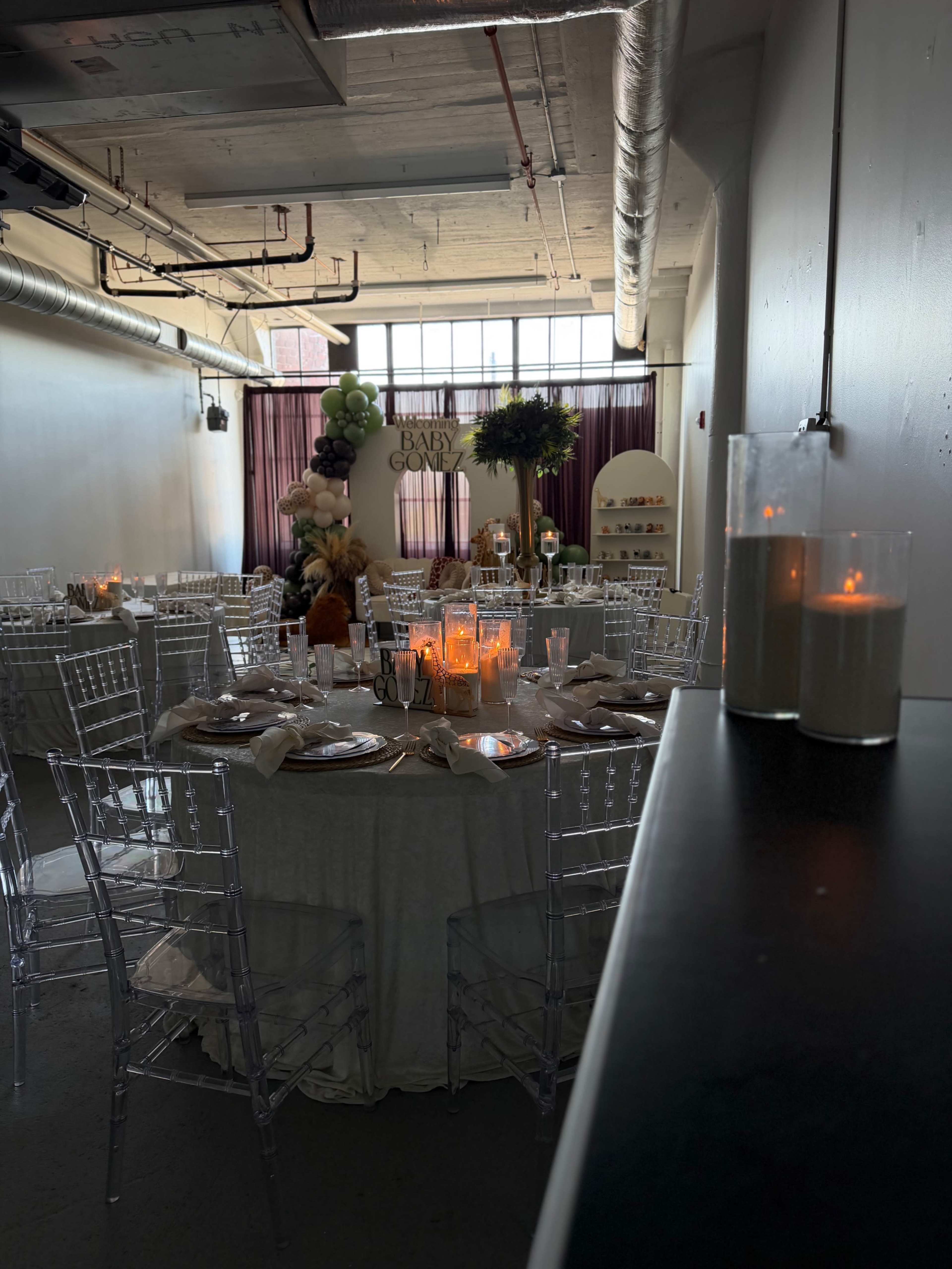 The image shows a decorated event space set up for a celebration, featuring tables with white tablecloths, candles, and decorative florals.