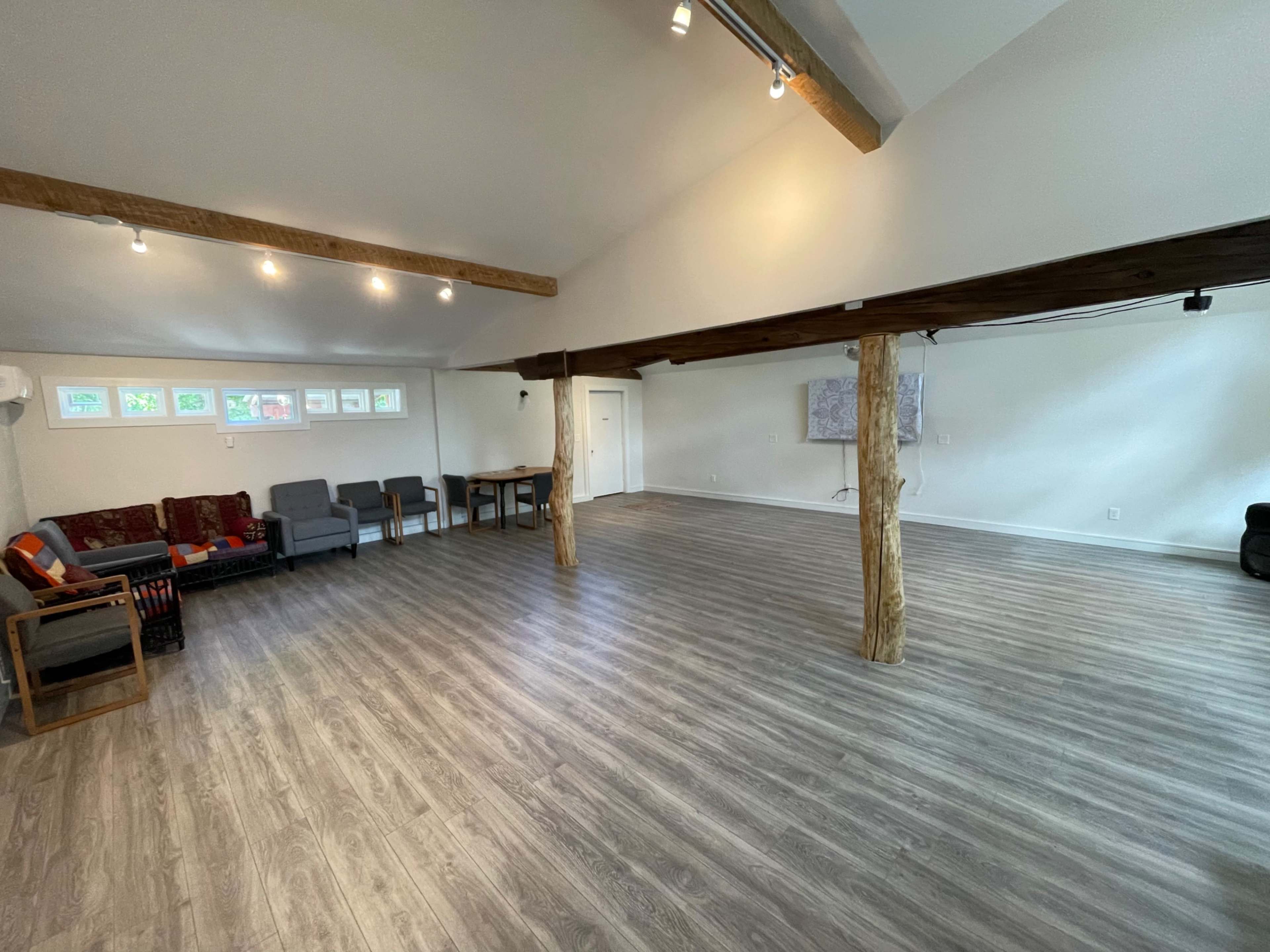 A spacious, well-lit interior with wooden beams, seating areas, and a wooden table in a minimalist design.