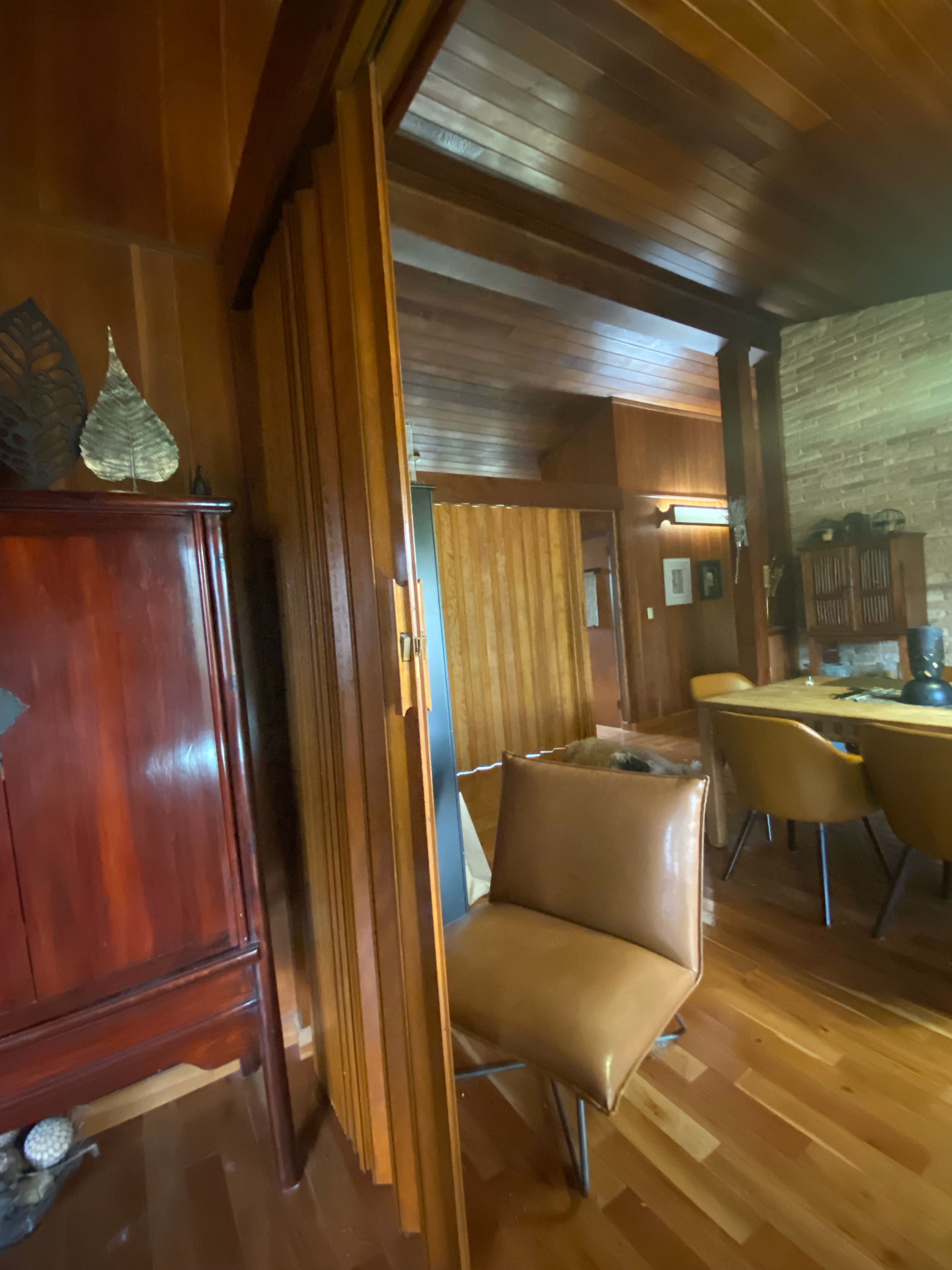 An interior space featuring wooden paneling, a brown chair, and a dining area in the background.