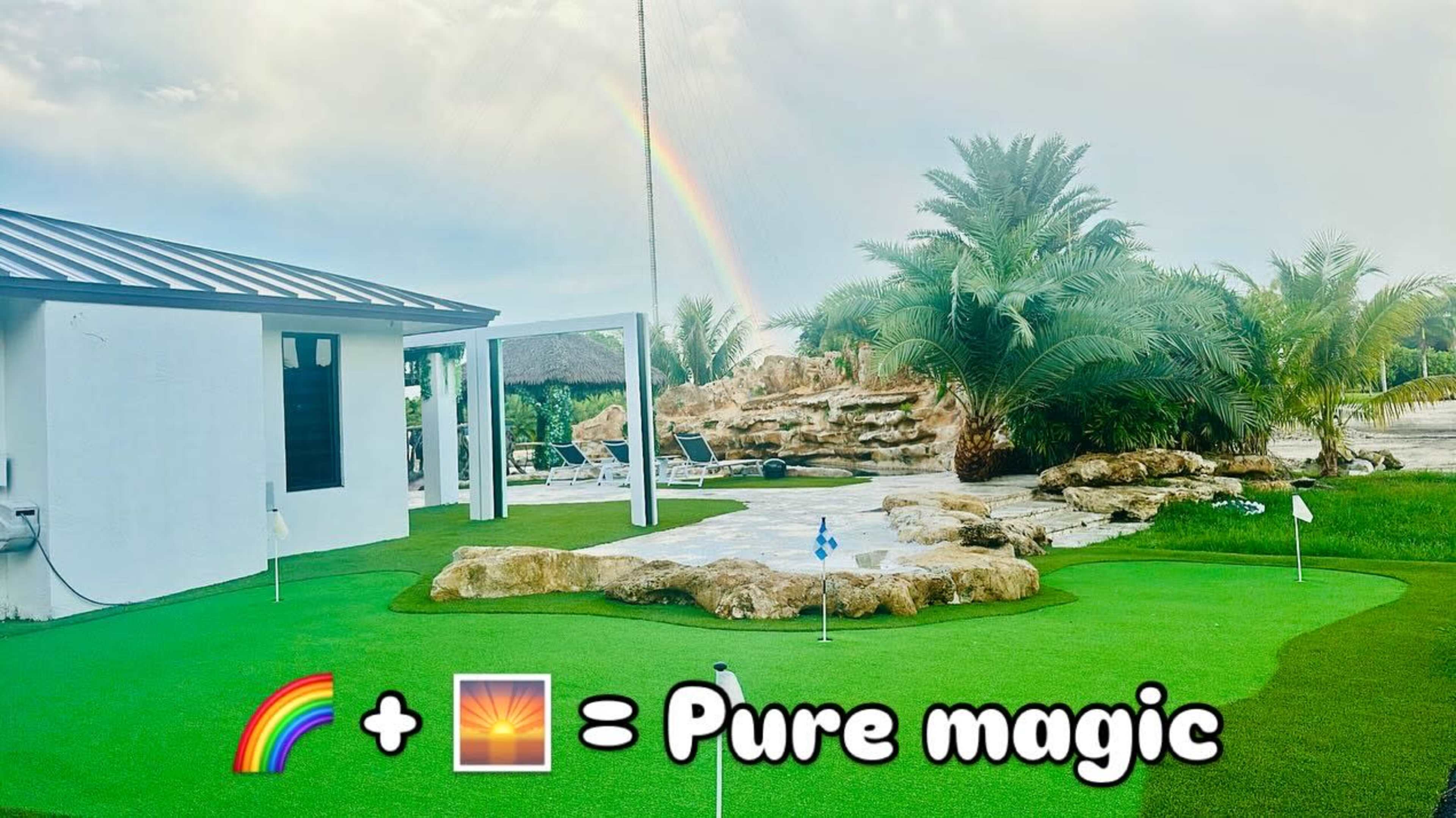 A vibrant green putting green is surrounded by palm trees and a rainbow arcs across the sky in the background.