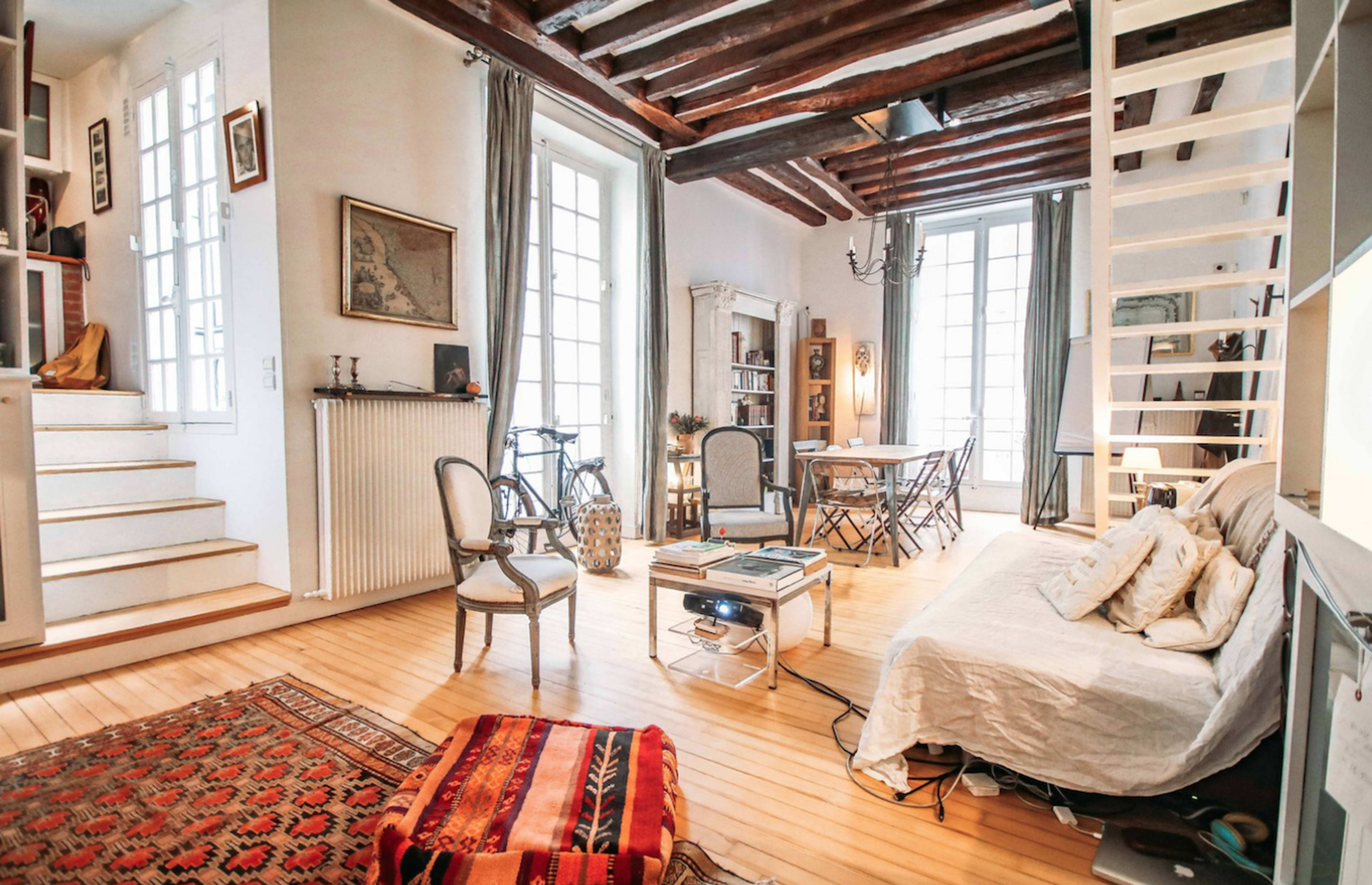 A spacious living area featuring wooden floors, a staircase, a seating area with a sofa, and a dining setup with chairs and a table.