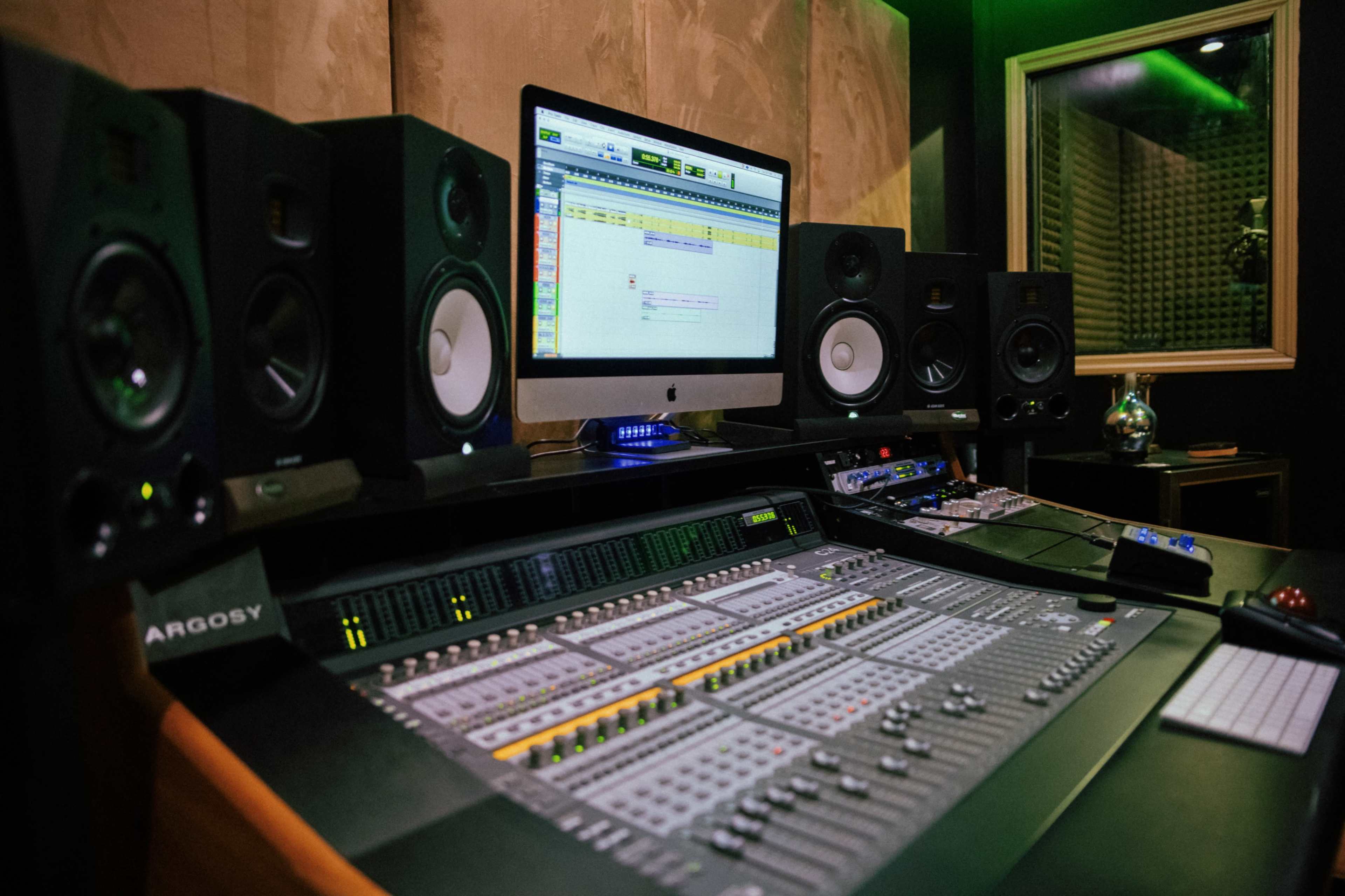 A music production studio featuring a digital audio workstation, mixing console, and multiple speakers.