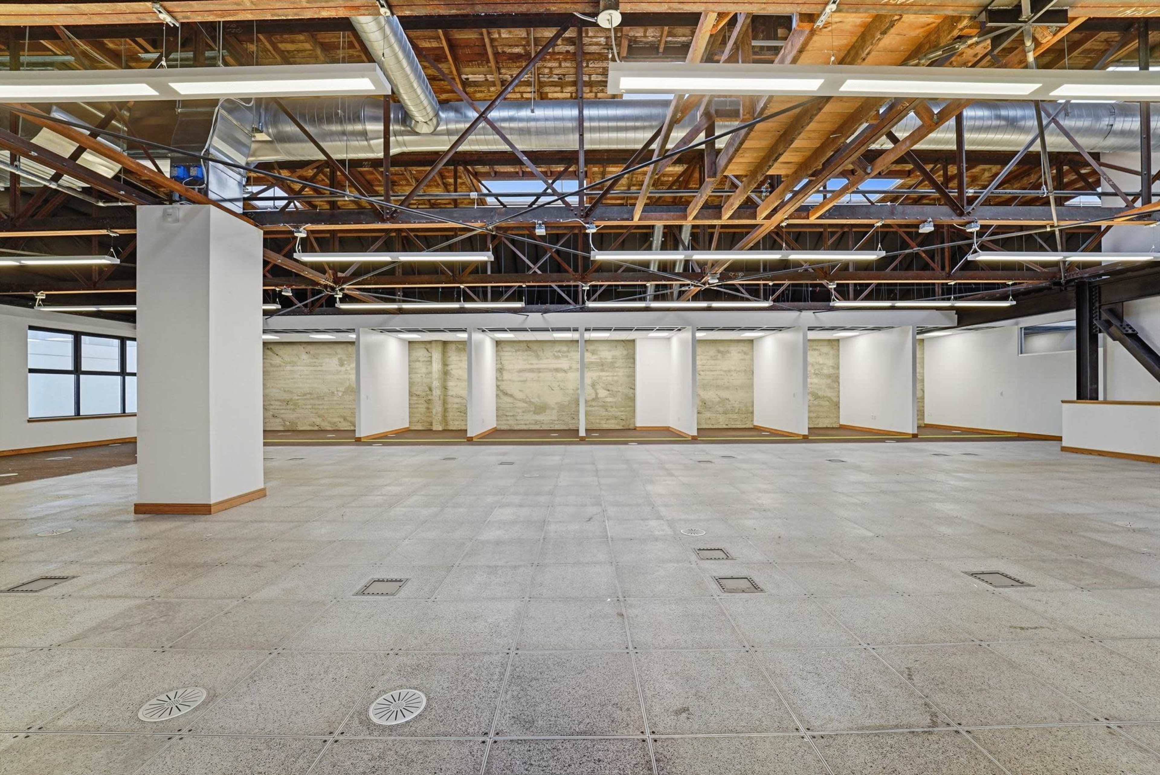 The image shows a spacious, empty room with high ceilings, exposed beams, and concrete flooring, featuring several adjustable wall panels.