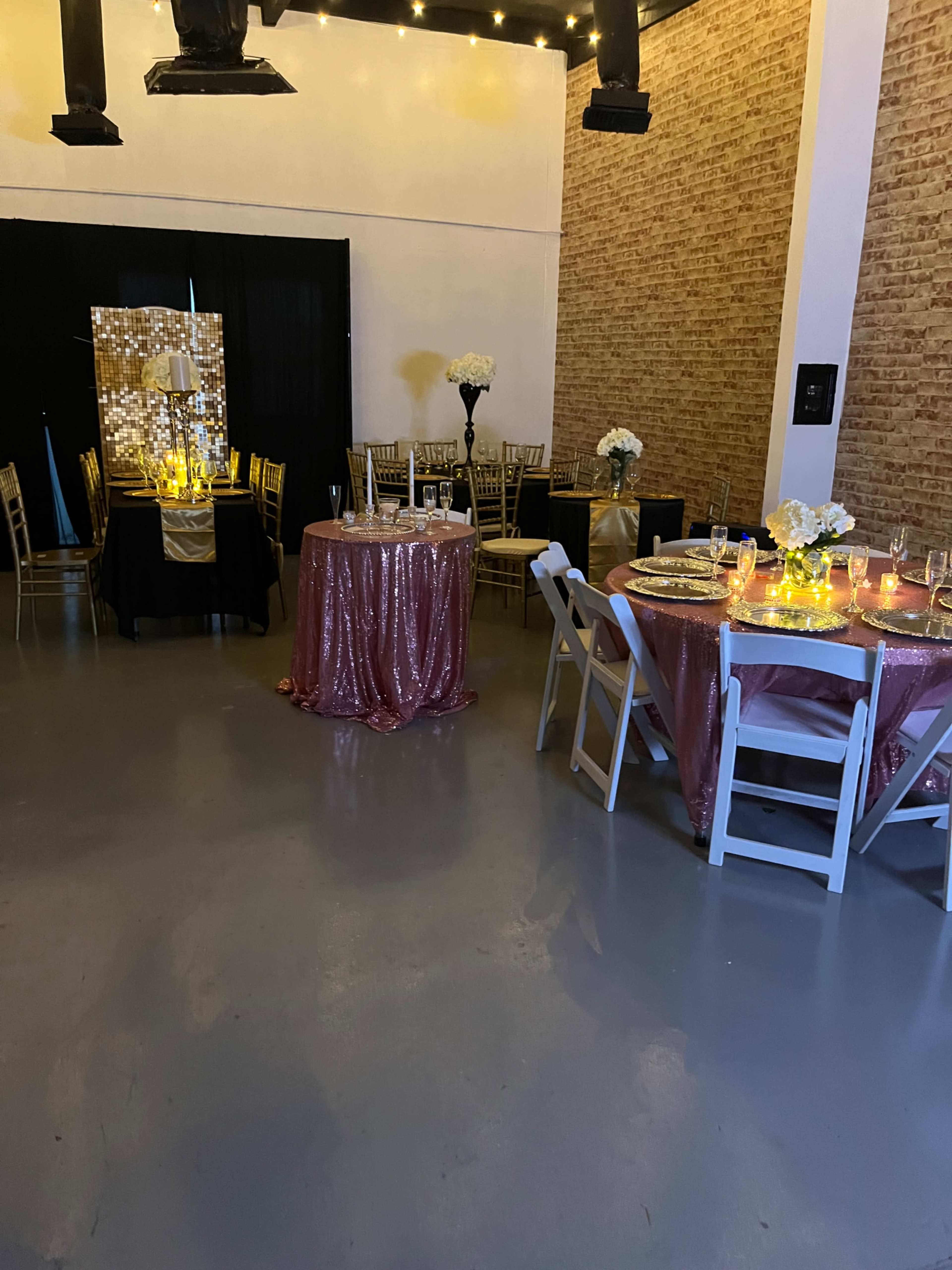 The scene features a decorated event space with tables covered in sparkling tablecloths, floral centerpieces, and ambient lighting against a backdrop of exposed brick walls.