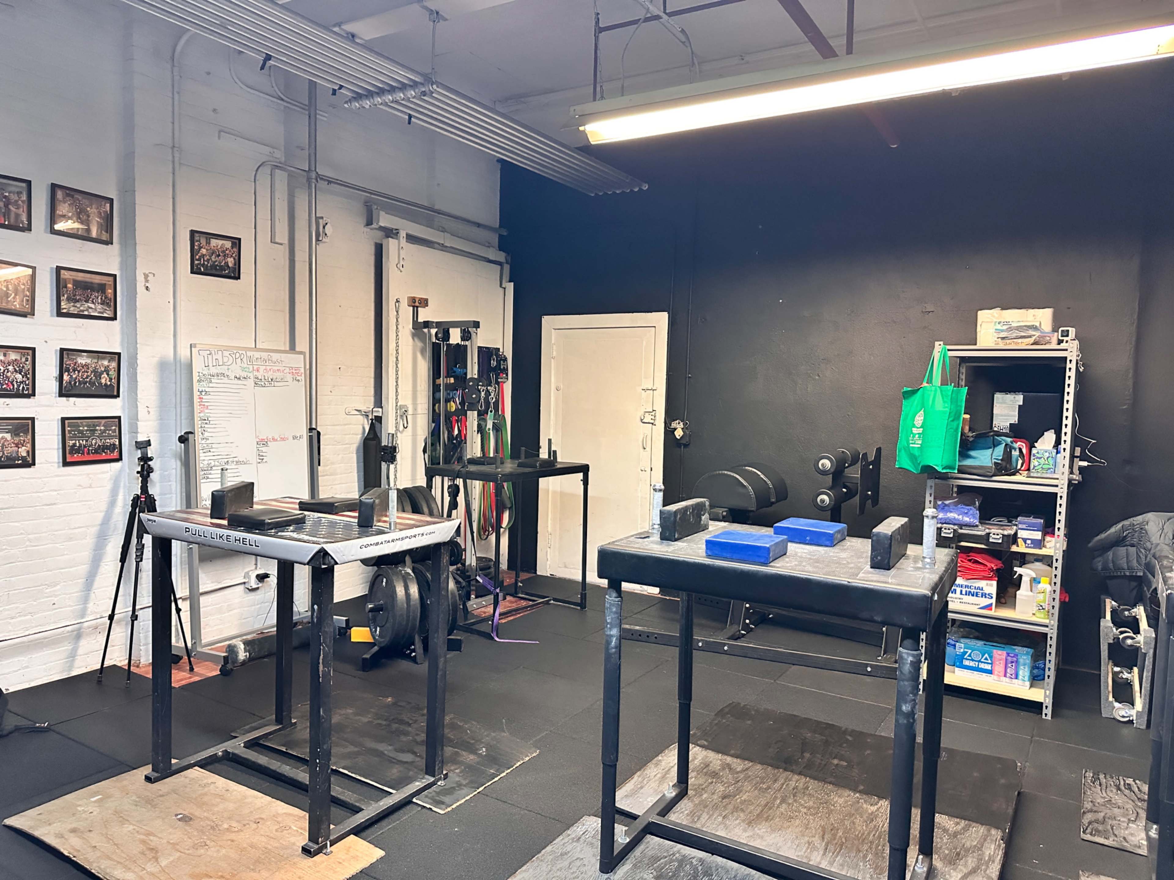 The image shows a gym interior with weightlifting equipment, including two benches and a shelving unit with various fitness supplies.